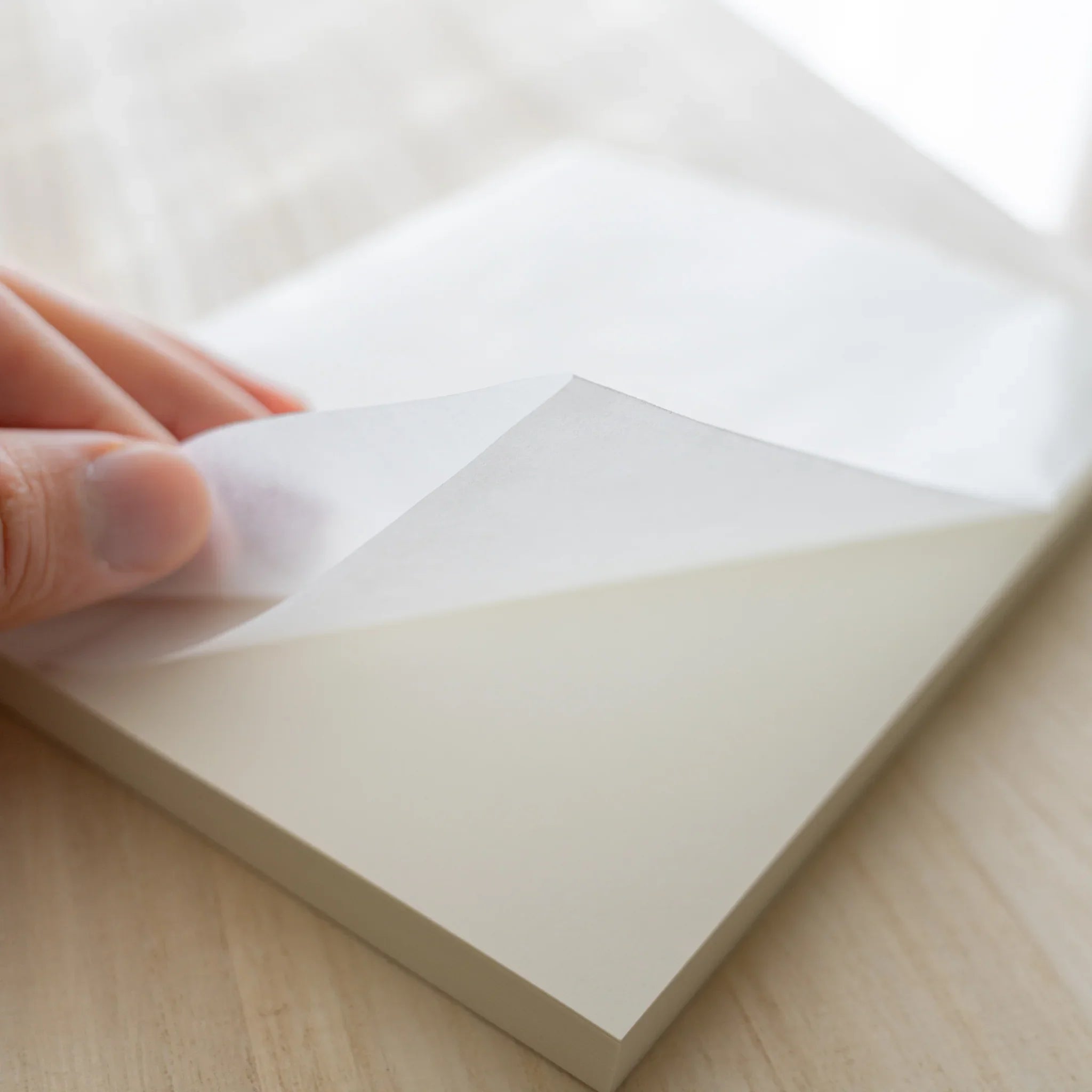 Hand lifting glassine wrapping off Midori MD Notebook A5, revealing ivory linen cover and page edges on wood surface
