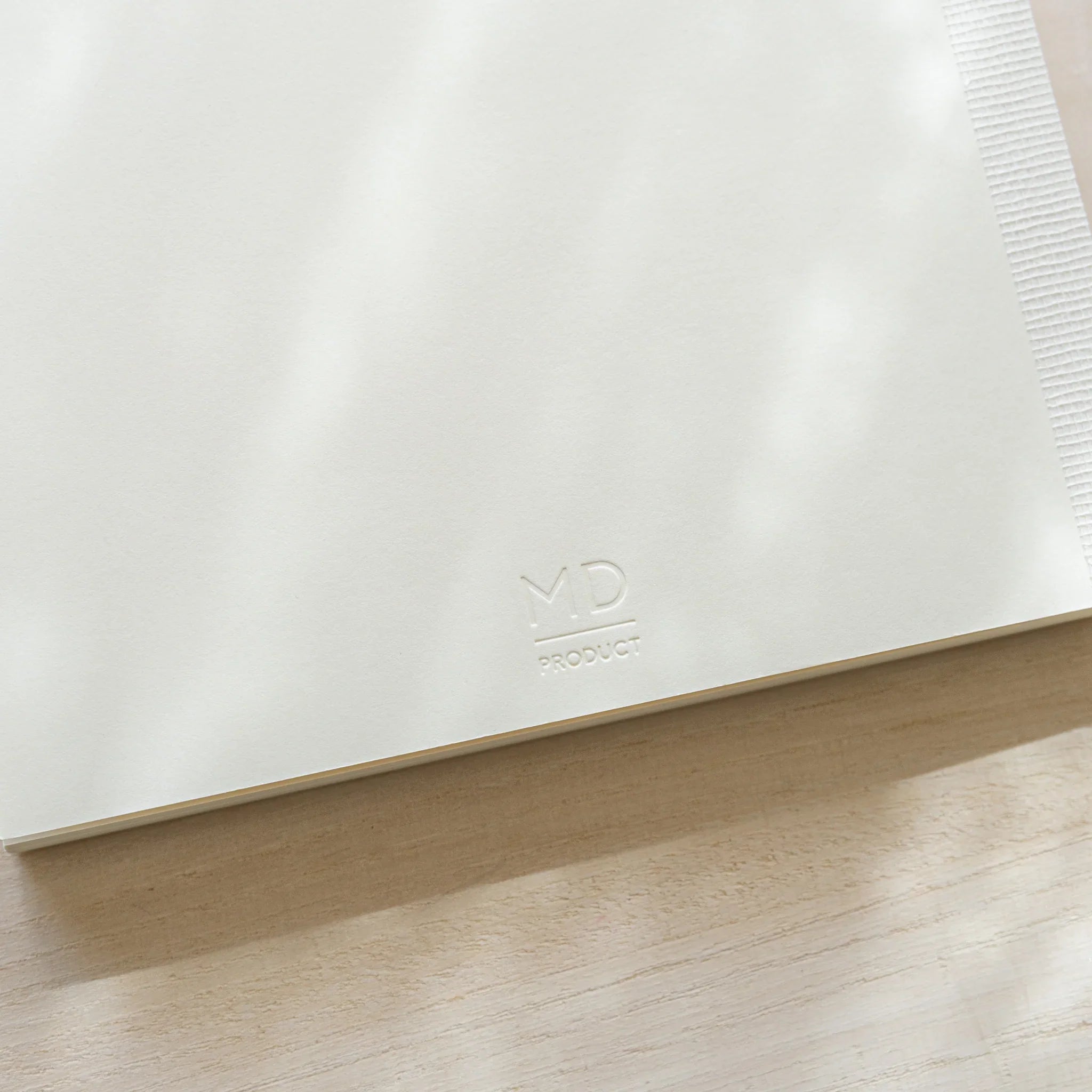 Close-up of Midori MD Notebook A5 lower corner with embossed MD Product logo on white linen cover and thread-stitched spine