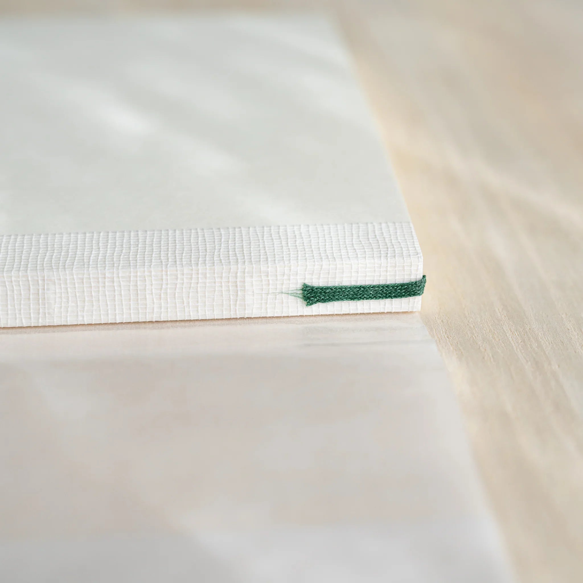 Close-up of Midori MD Notebook A5 white linen cover side showing dark green ribbon bookmark extending from spine on wood
