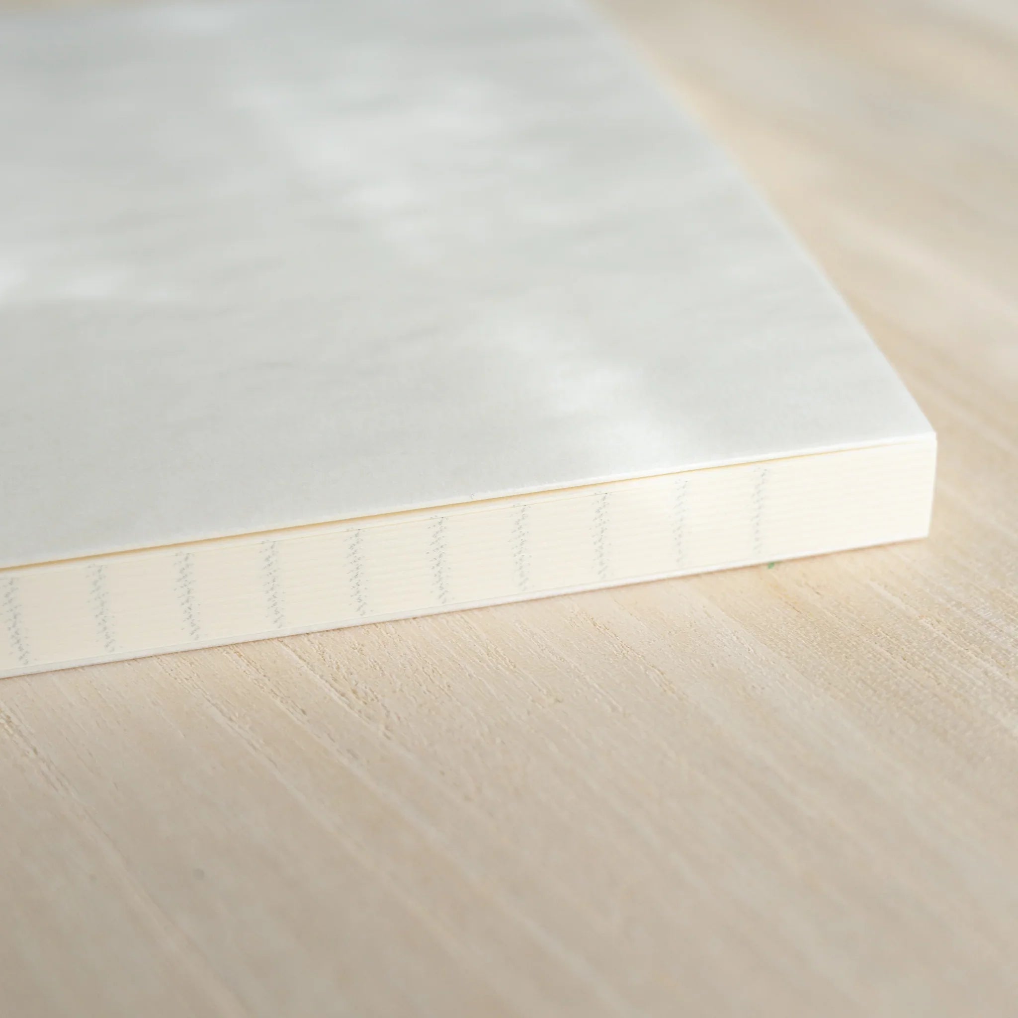 Closed Midori MD Notebook A5, angled view showing white linen cover, ivory page edges, and dark green satin ribbon