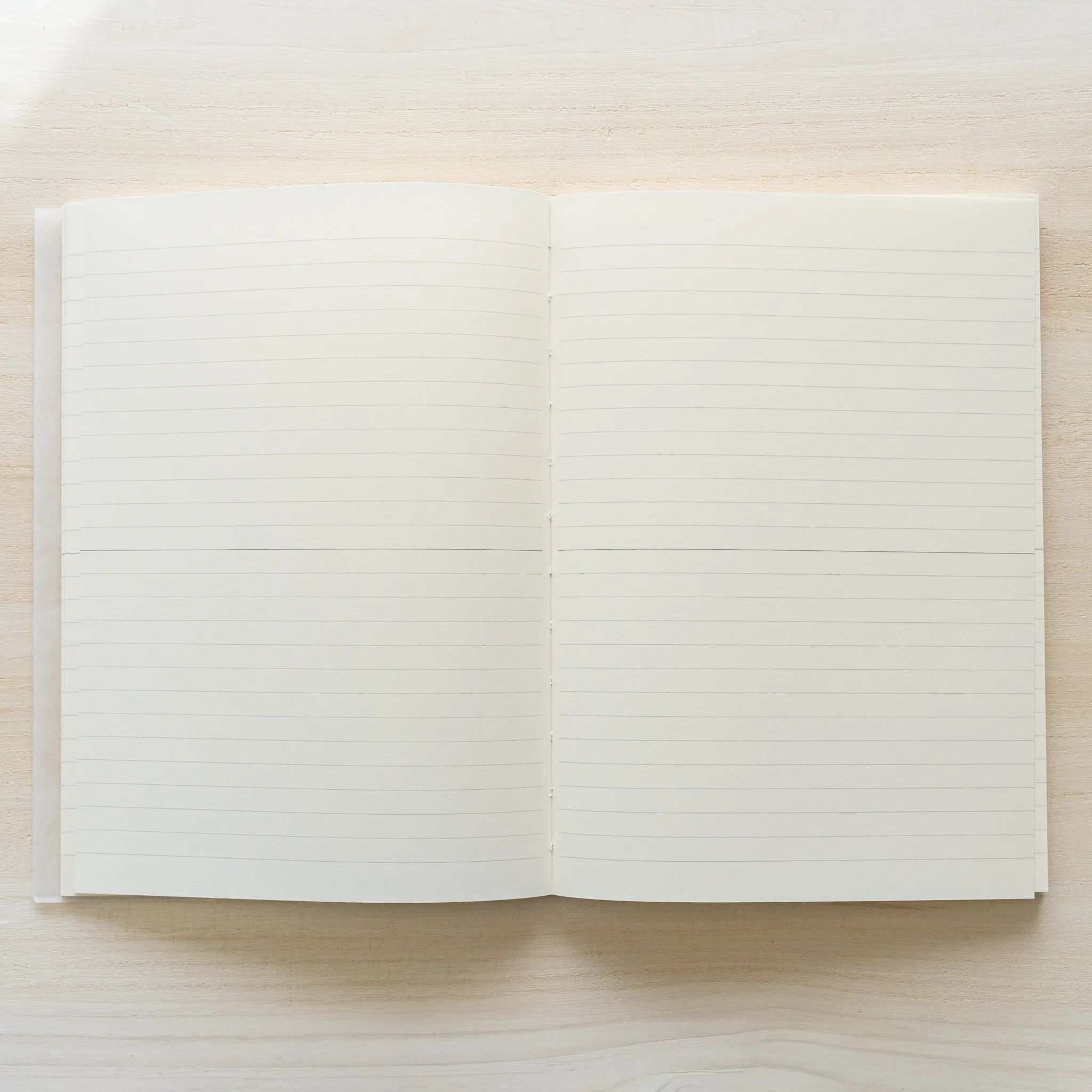 Midori MD Notebook A5 opened flat to lined ruling spread, both pages showing ivory paper with horizontal lines, center spine