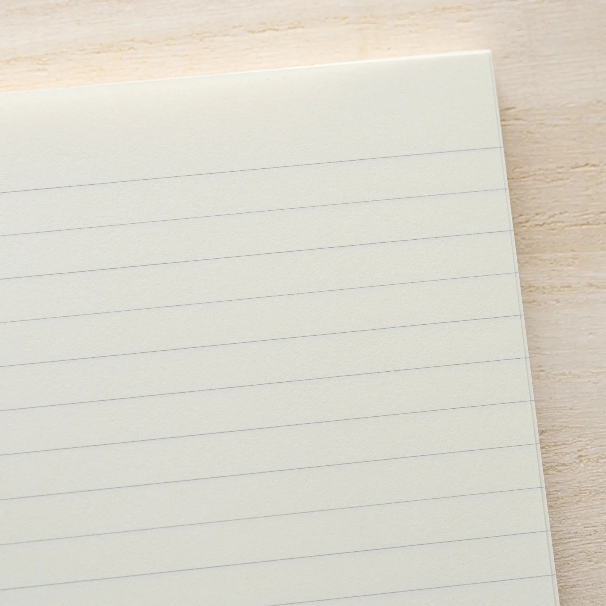 Midori MD Notebook A5 lined page close-up showing ivory paper with horizontal ruling and rounded corner on wood surface