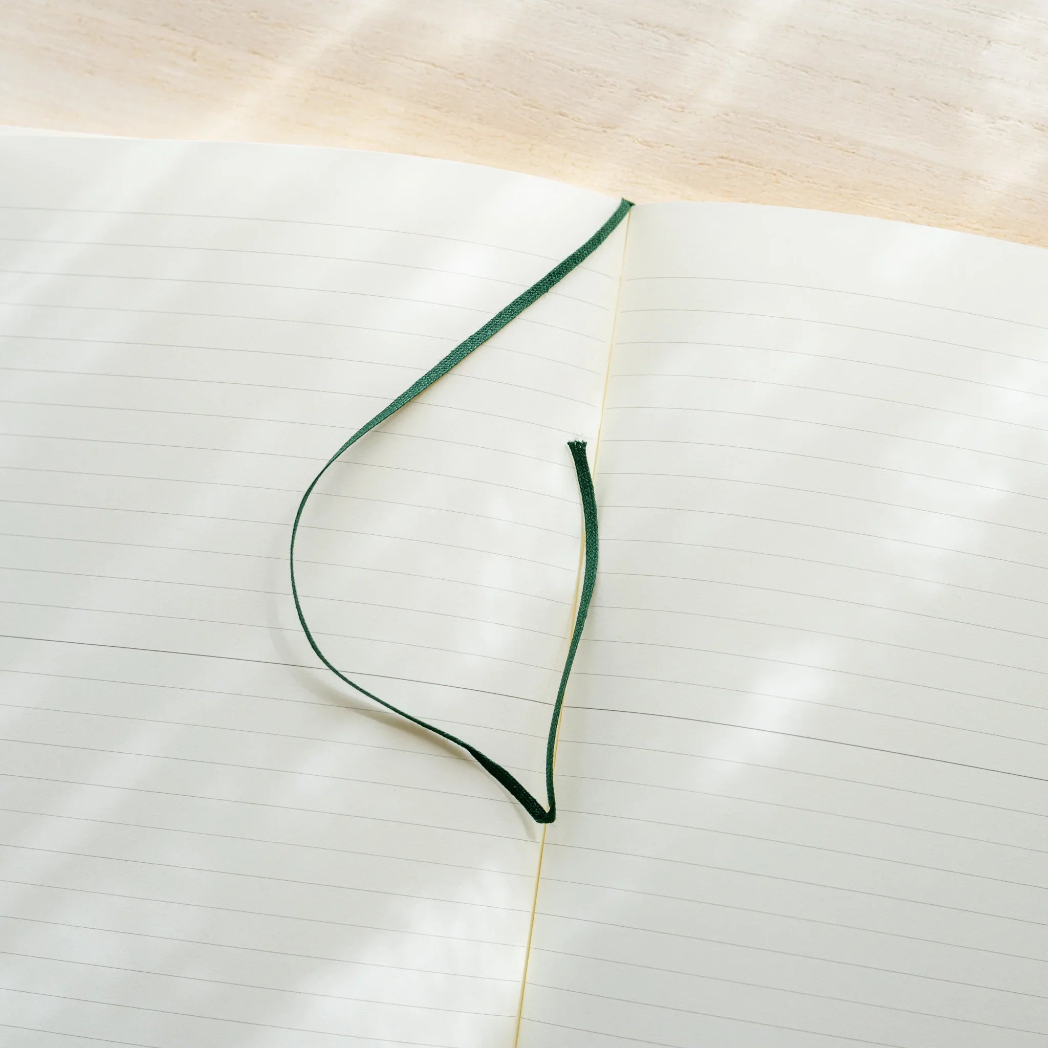 Midori MD Notebook A5 opened to ivory lined spread, dark green ribbon bookmark curled on left page, center spine visible