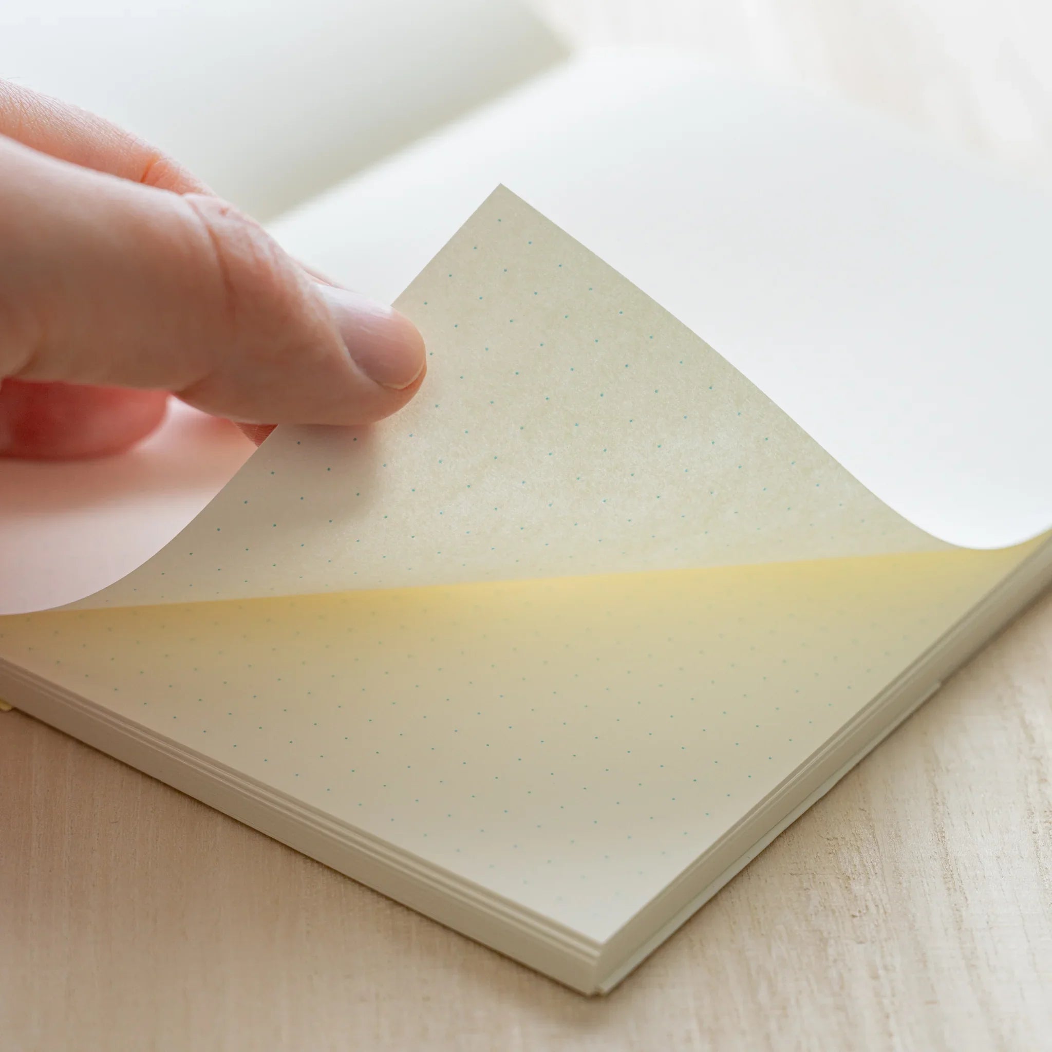 Hand turning ivory dot grid page of Midori MD Notebook A5, showing warm ivory paper tone and page thickness