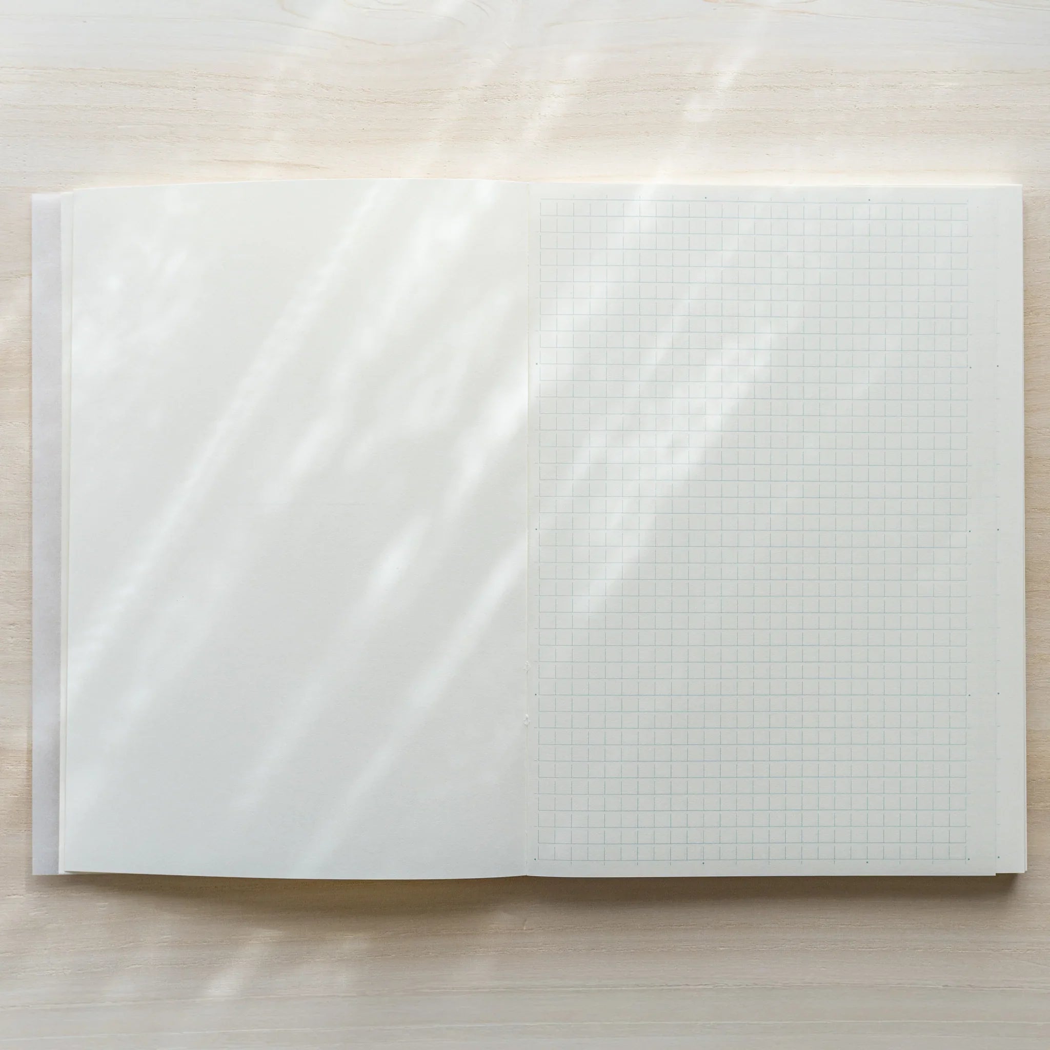 Midori MD Notebook A5 opened flat from above, left page blank white, right page showing grid ruling, center spine on wood