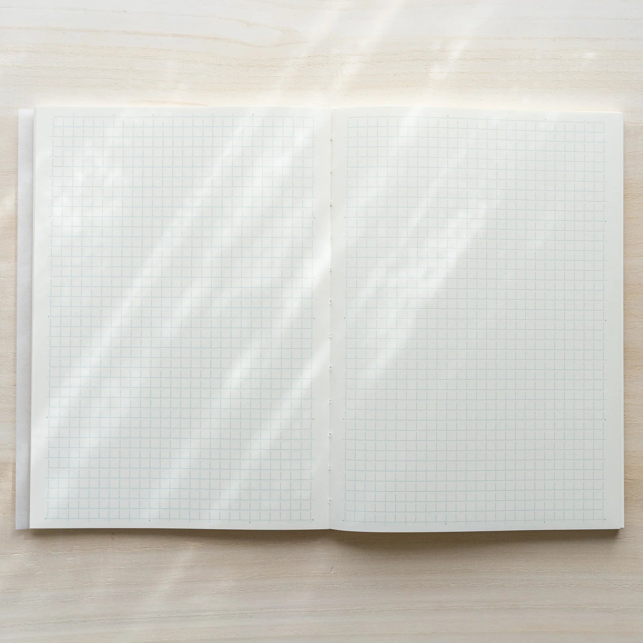 Midori MD Notebook A5 opened flat to grid ruling spread, both pages showing white grid lines, center spine visible on wood