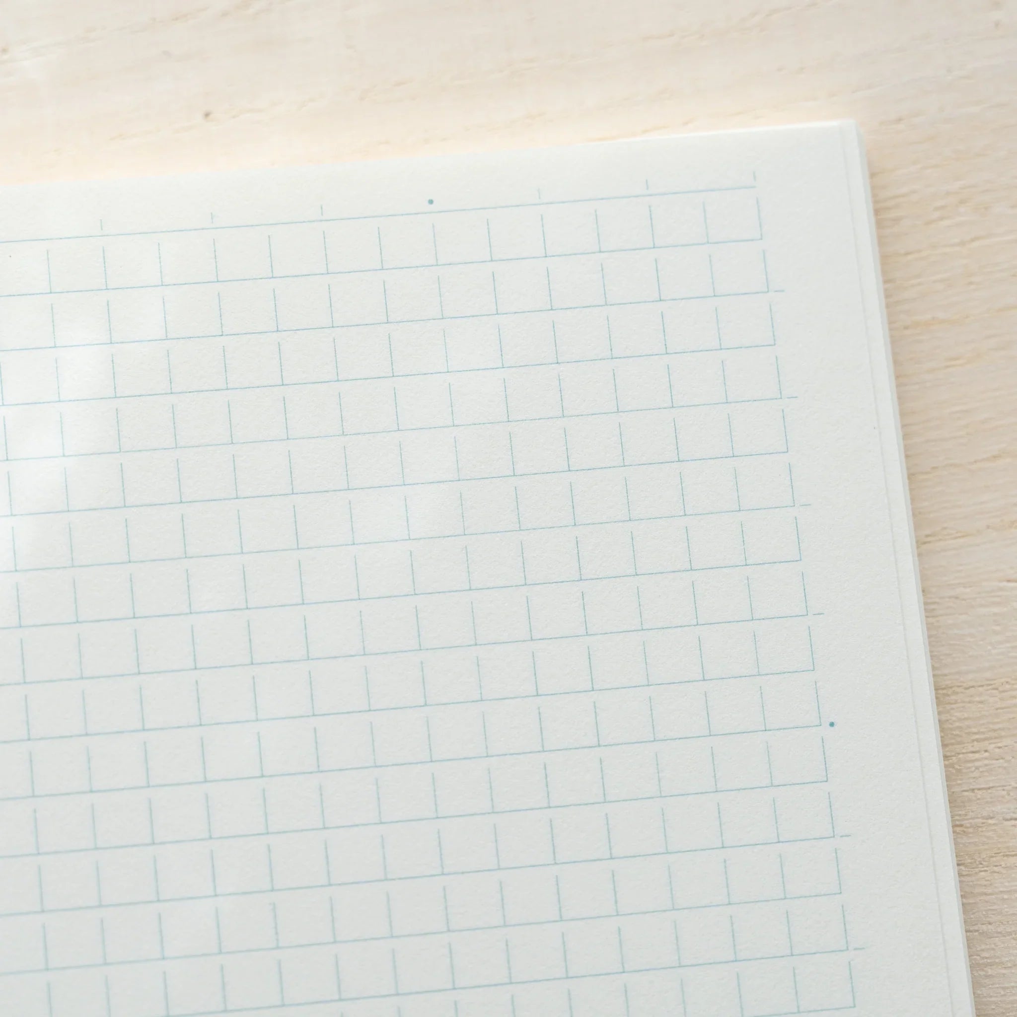 Midori MD Notebook A5 grid page close-up showing white paper with light blue grid lines and rounded corner on wood surface