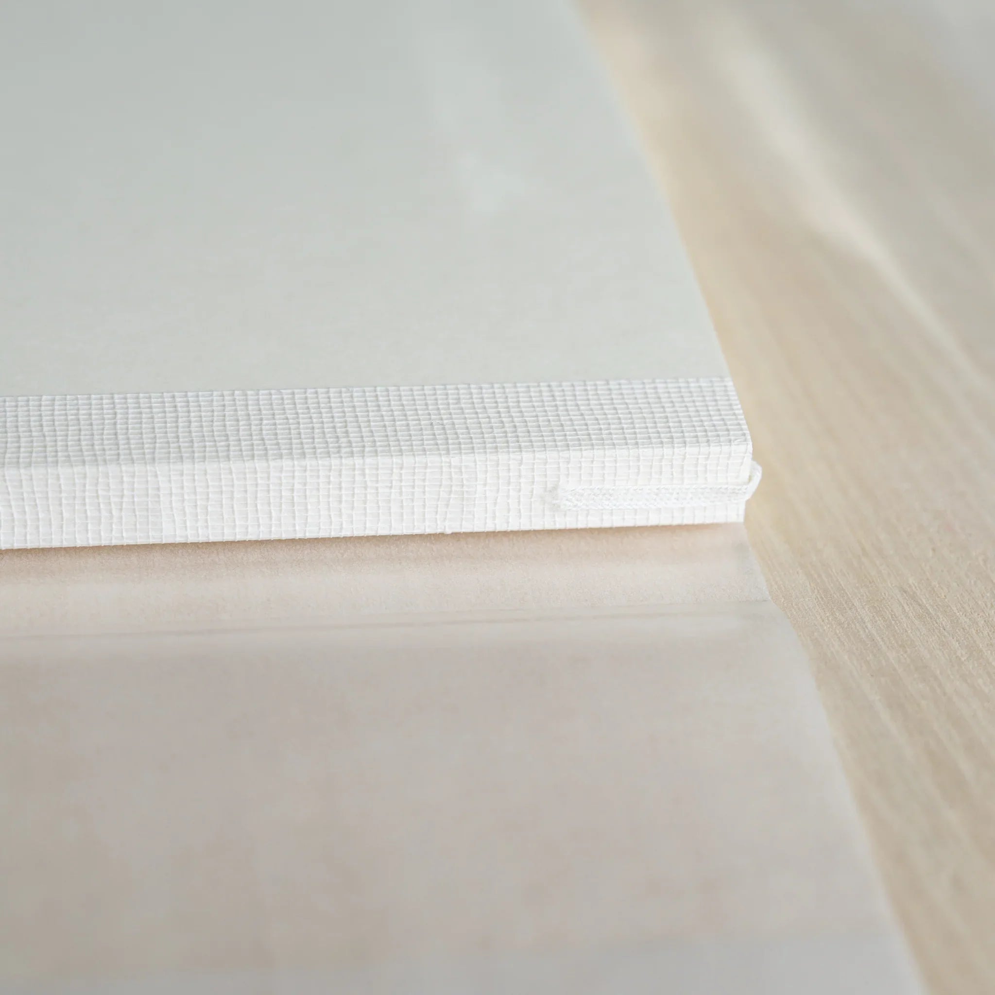 Closed Midori MD Notebook A5, angled view showing white linen cover, ivory page edges, and white ribbon bookmark at corner