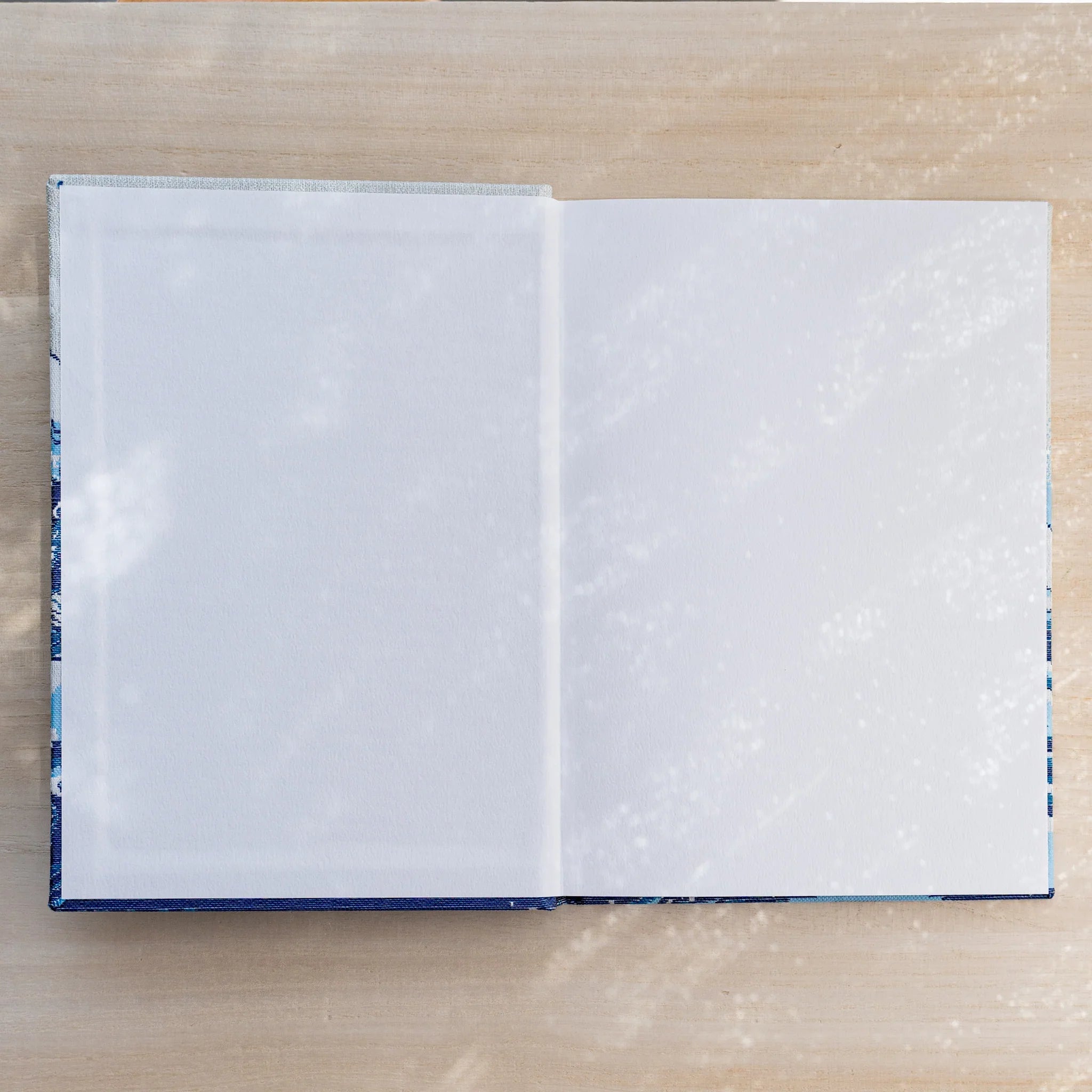 Notebook opened flat to two blank white pages, blue patterned textile inner cover visible at the edges