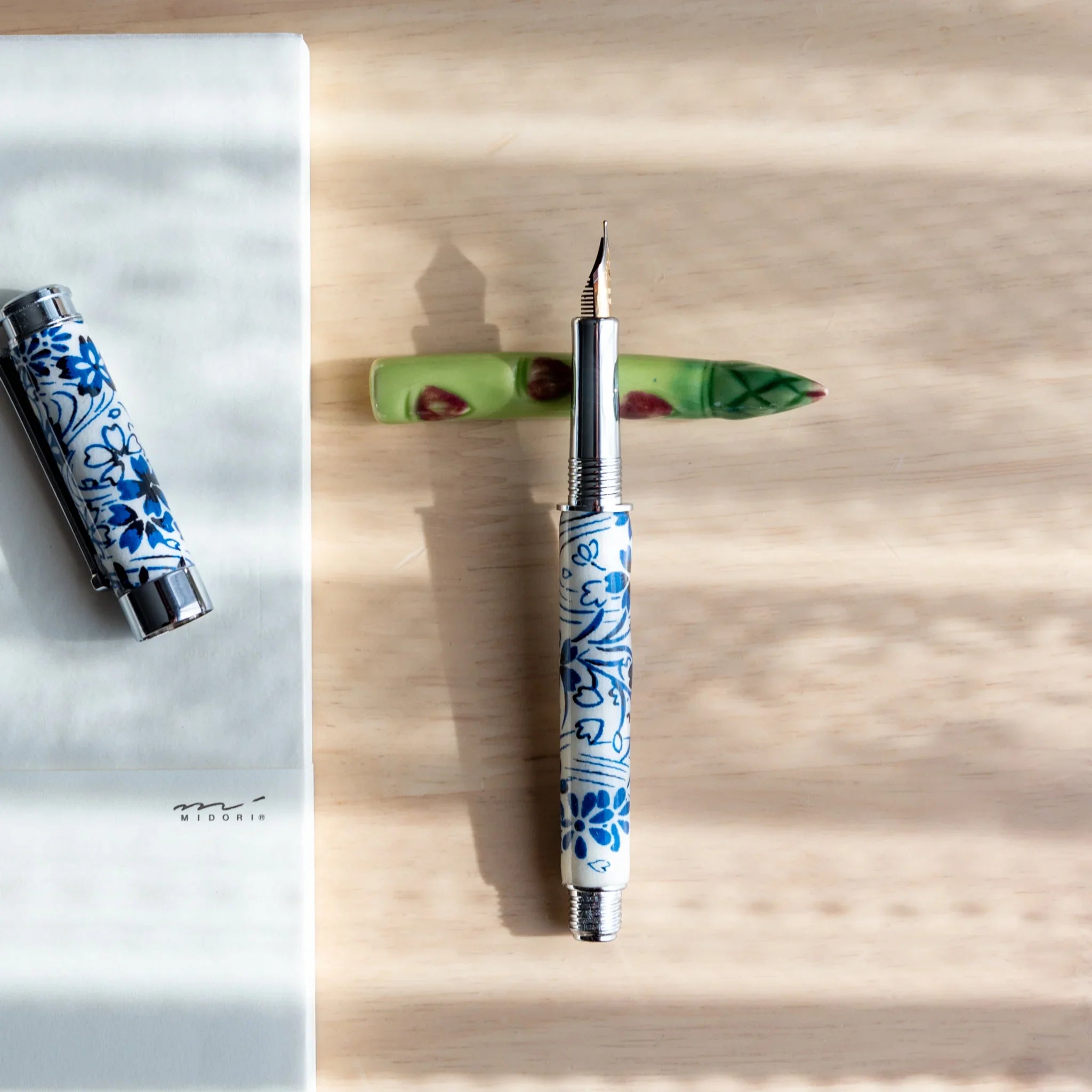 Olive green asparagus-shaped handcrafted pen rest with natural texture and recessed functional groove on neutral surface