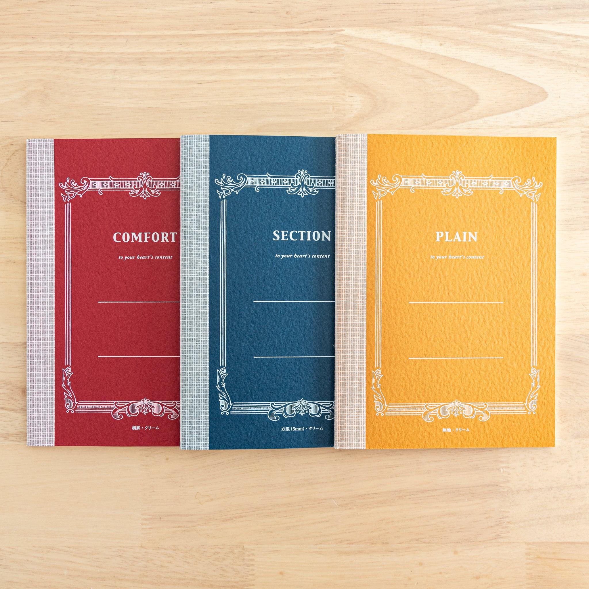 Three Tsubame Japanese notebooks on a wooden surface, labeled "Comfort," "Section," and "Plain," featuring elegant vintage-style covers. A classic piece of Japanese stationery.