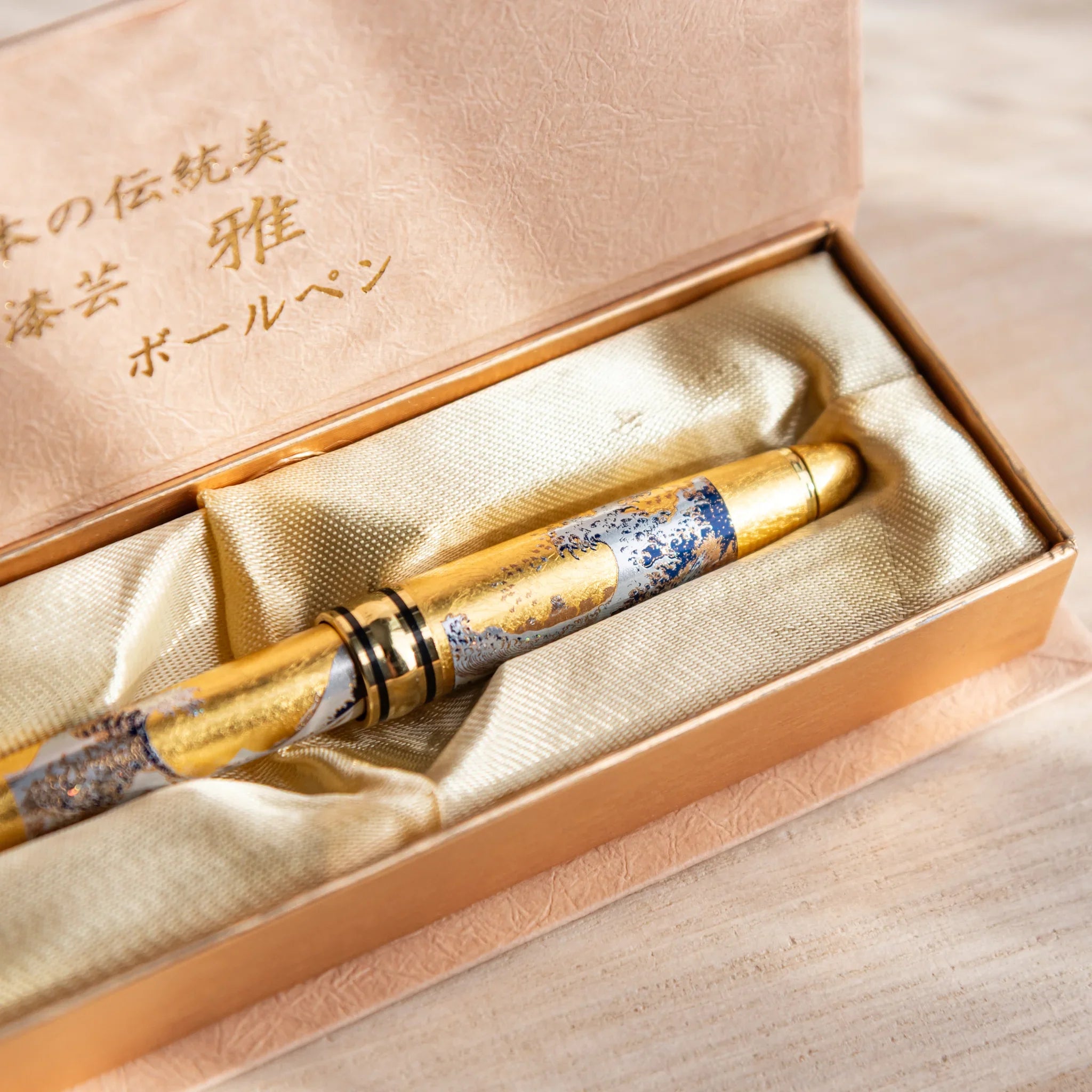 Gold Leaf Great Wave Japanese Ballpoint Pen in a satin-lined gold gift box, showing blue wave art and a shimmering gold body.”