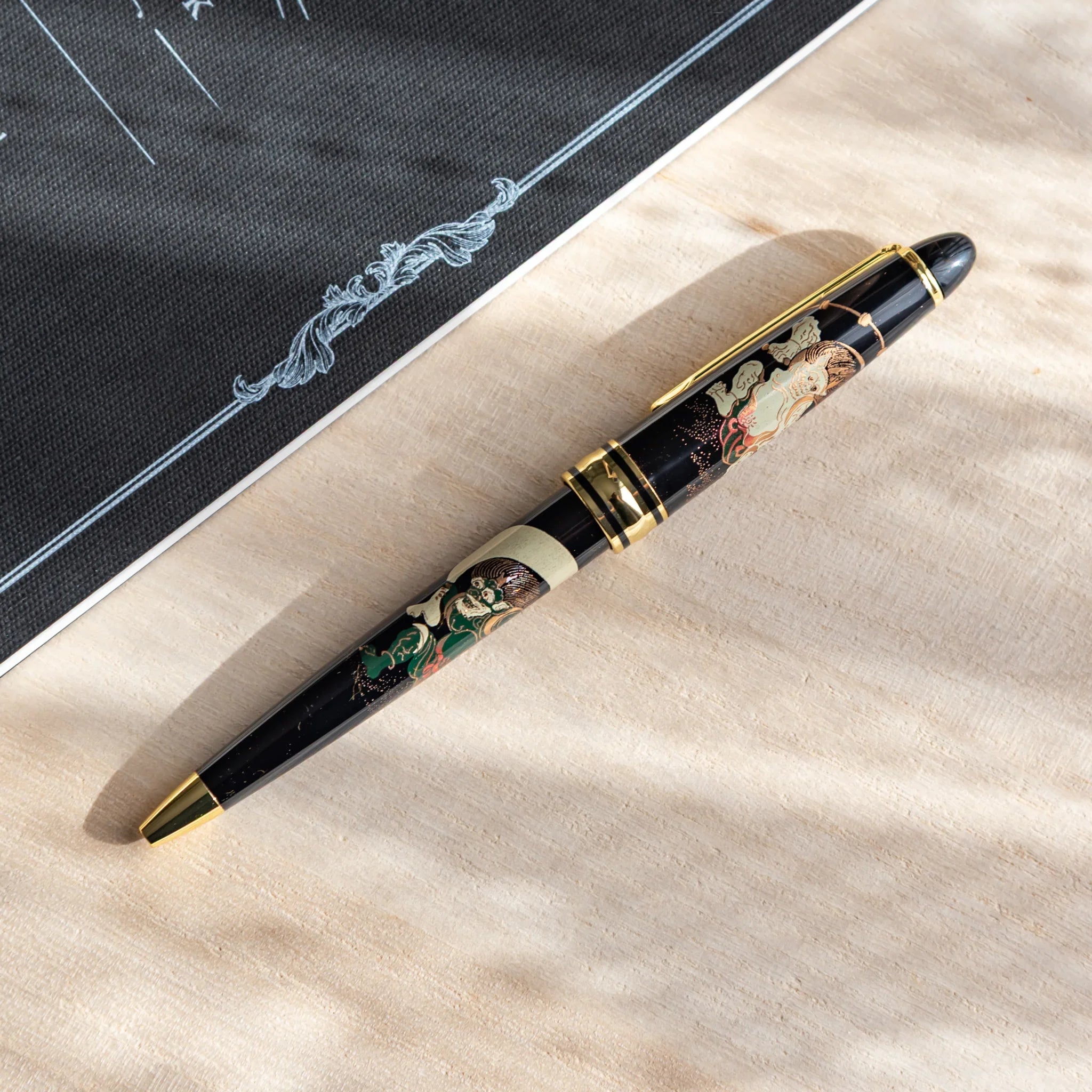 Gods of Wind and Thunder Yamanaka retractable ballpoint pen with black barrel and maki-e decoration displayed clearly