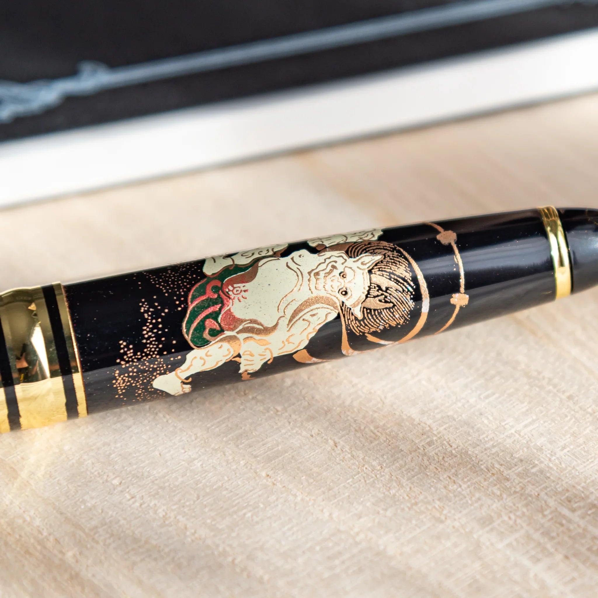 Black ballpoint pen with gold accents and traditional deity motif lacquerware decoration displayed clearly