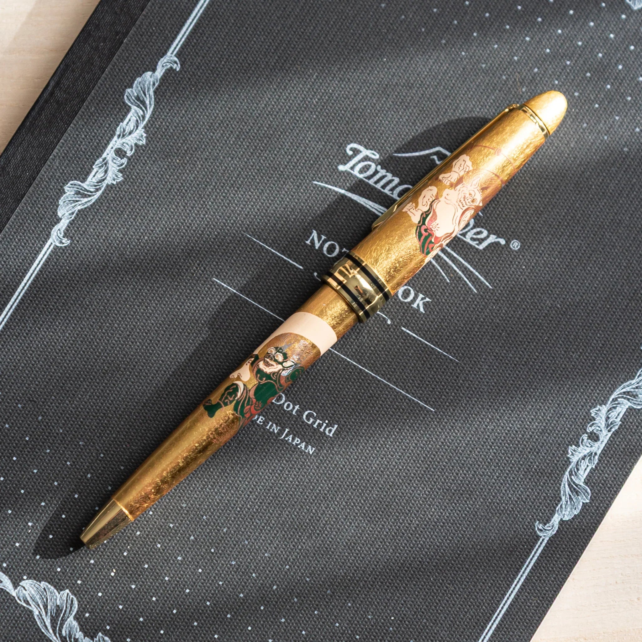 Black ballpoint pen with gold trim and ornate maki-e artwork of traditional deities displayed clearly