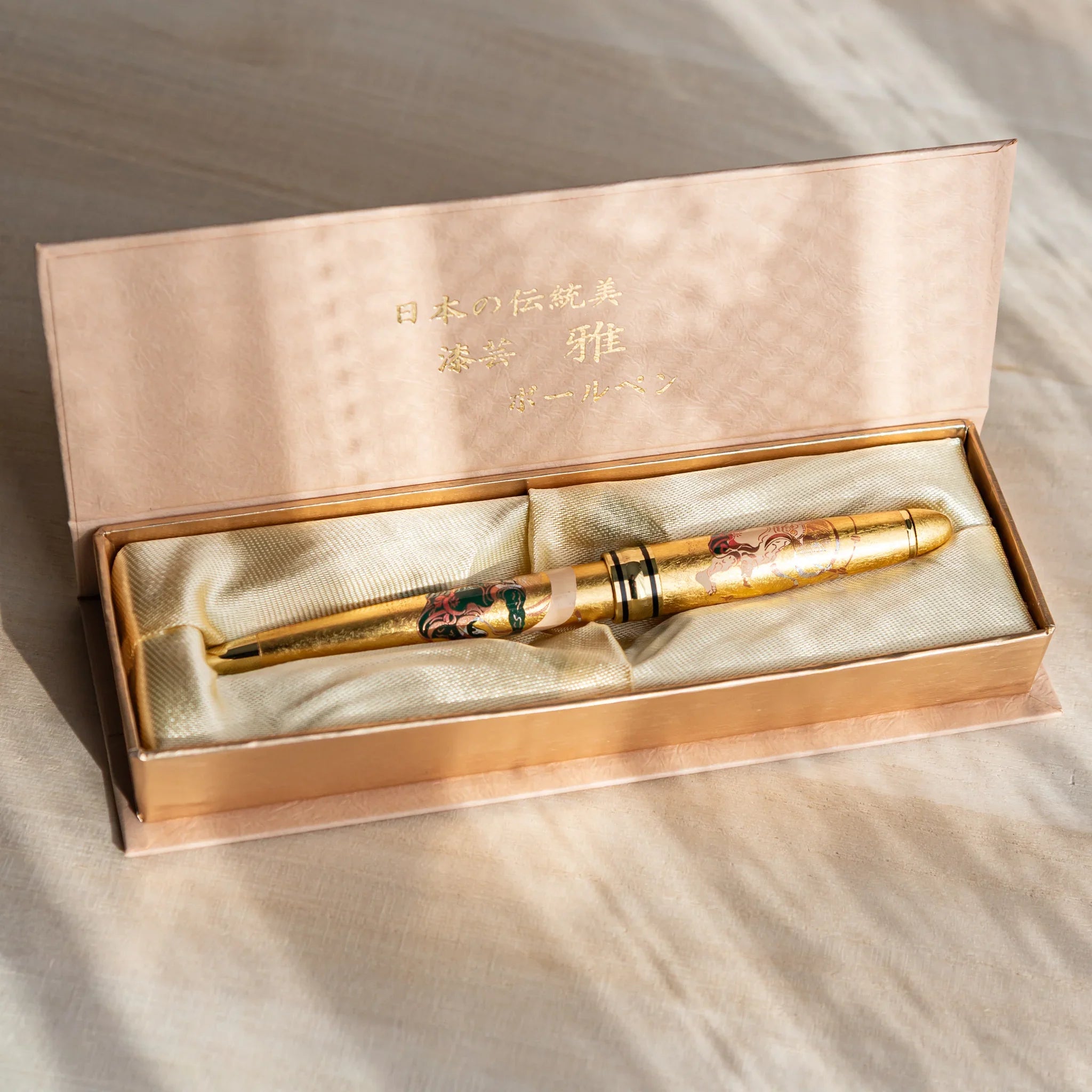 Gift box displaying a gold leaf Japanese Ballpoint Pen with Raijin and Fujin design, set in a satin-lined case under warm light.