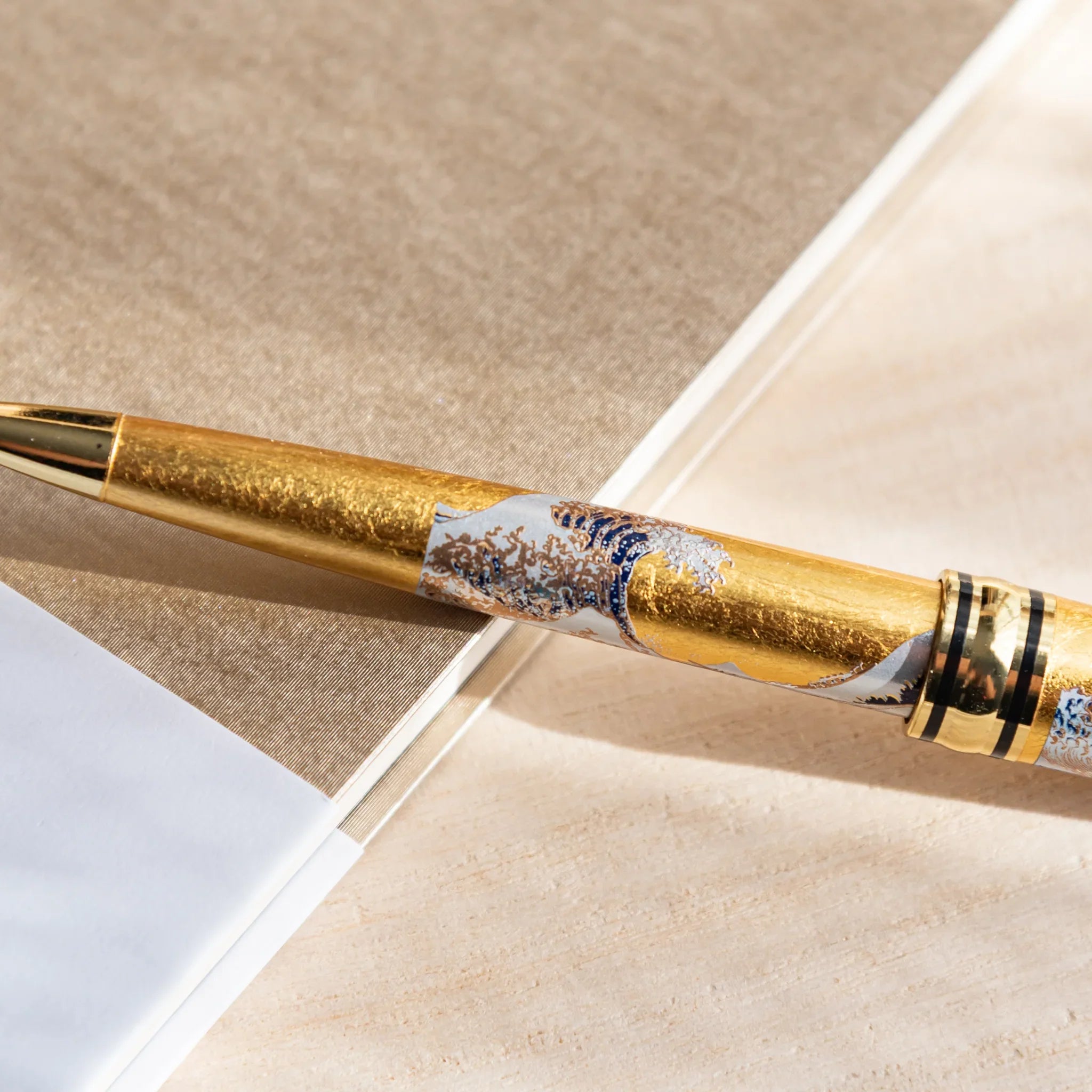 Gold Leaf Great Wave Japanese Ballpoint Pen on layered notebooks, showing blue-and-gold wave art and gold leaf details.