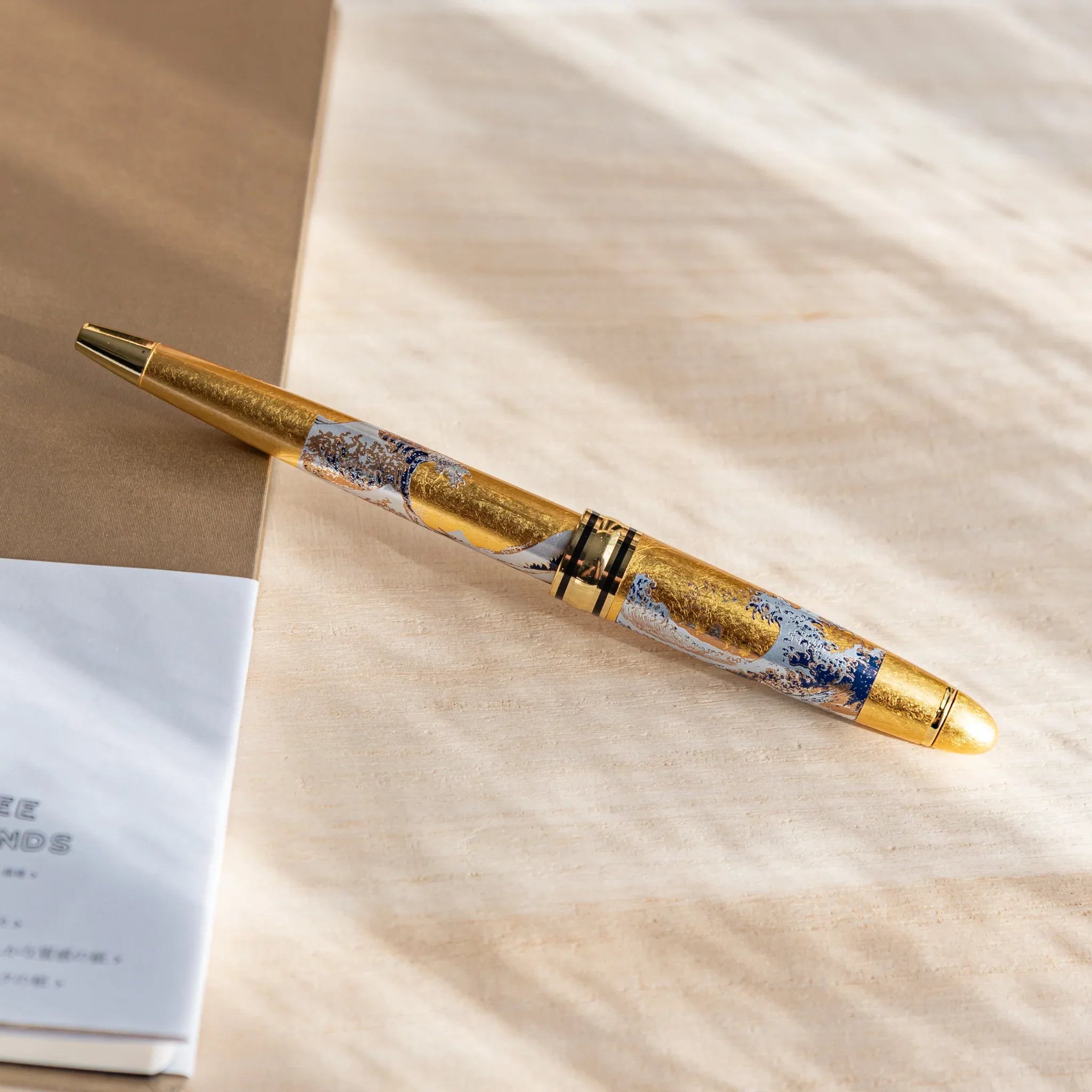 Hokusai Great Wave ballpoint with ornate gold accents on dark lacquer surface shown in composition composition shown