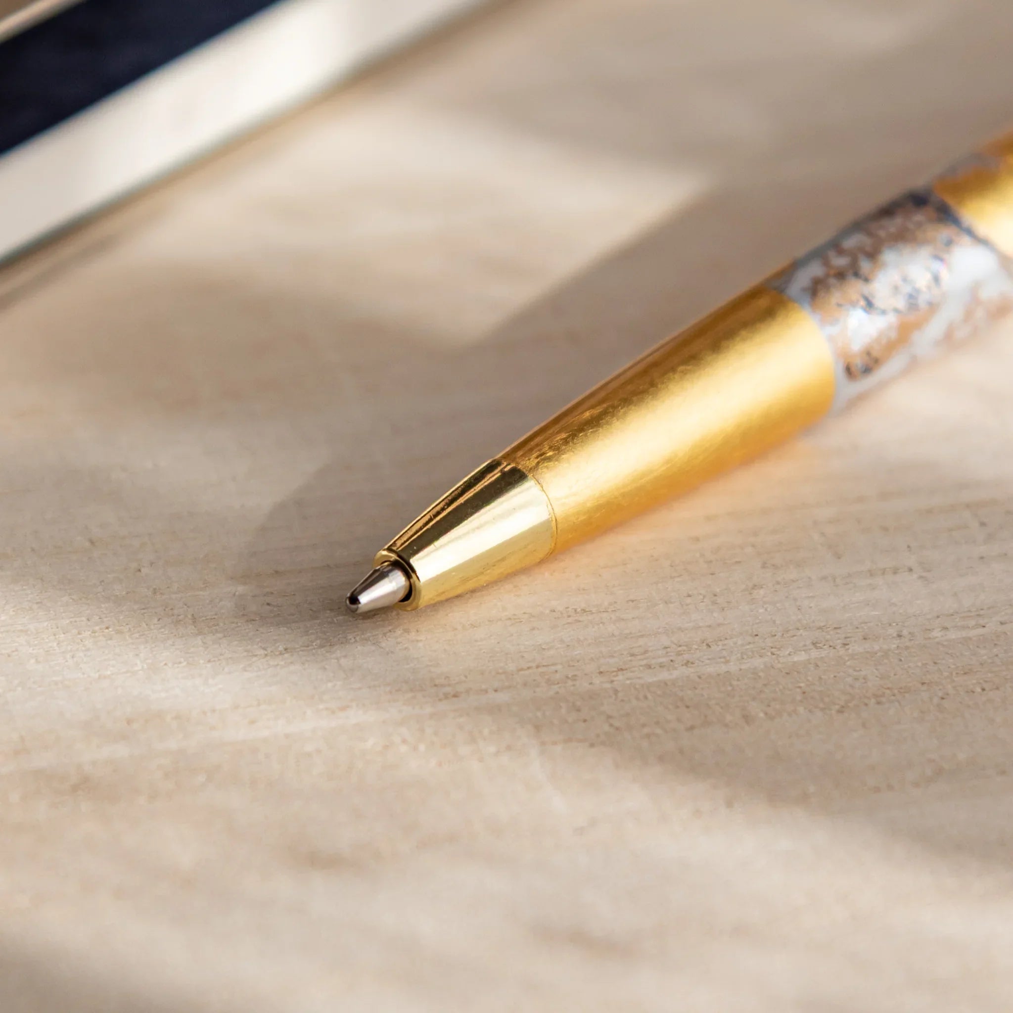 Gold Japanese Ballpoint Pen tip on a light wood desk, featuring a smooth gold cone and subtle Great Wave gold-leaf detail.