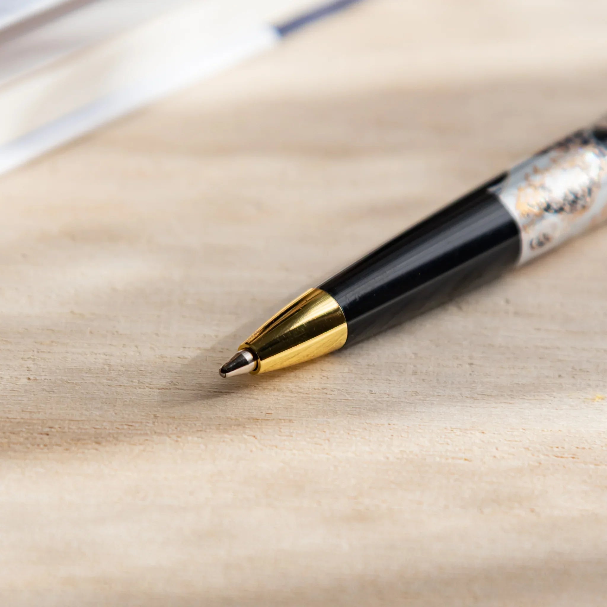 Japanese Ballpoint Pen tip resting on a desk, showing a gold cone tip, black barrel, and silver Great Wave design near the grip.