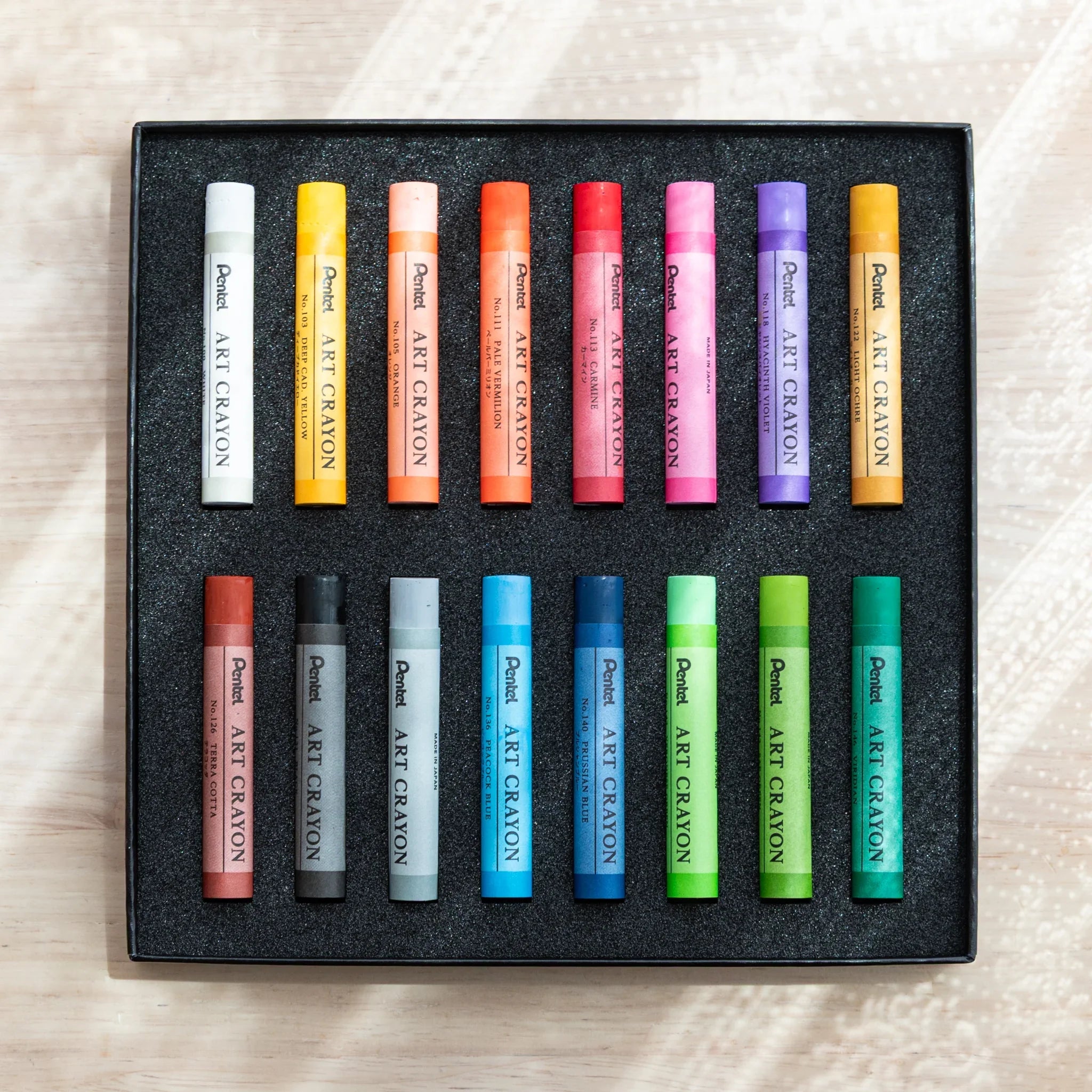 Open Pentel Art Crayon 16-color box viewed from above showing all 16 sticks in two rows of 8 in a black foam tray