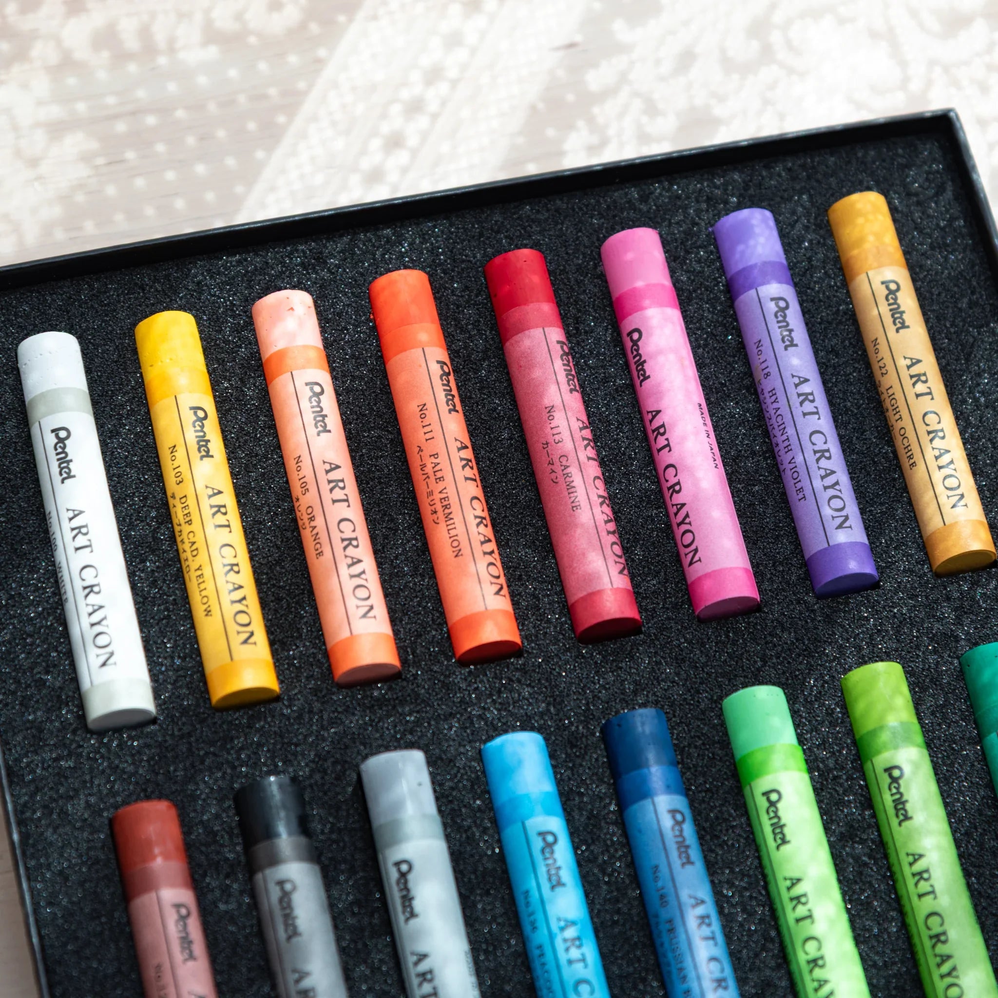 Pentel Art Crayon 16 Colors box open at an angle, upper row showing Deep Cad Yellow, Orange, Carmine, and Hyacinth Violet
