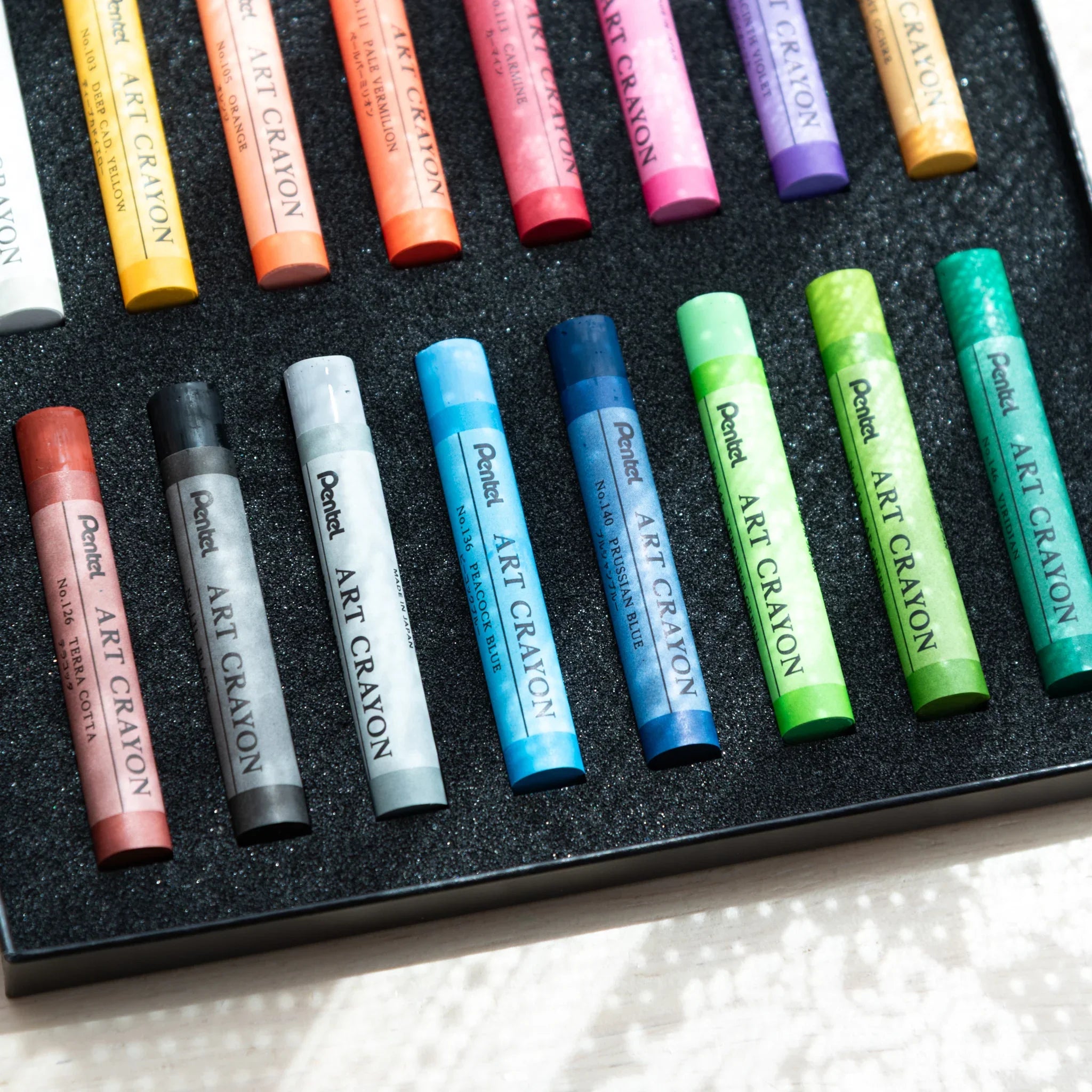 Lower row of Japanese crayon set by Pentel showing individual colored art crayons neatly arranged in a black foam tray inside the box