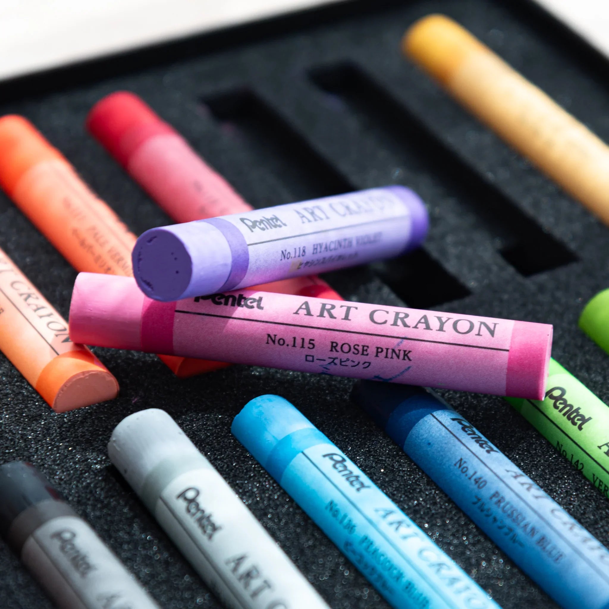 Japanese crayon set by Pentel with rose pink crayon and other colored art crayons lying on foam tray inside box