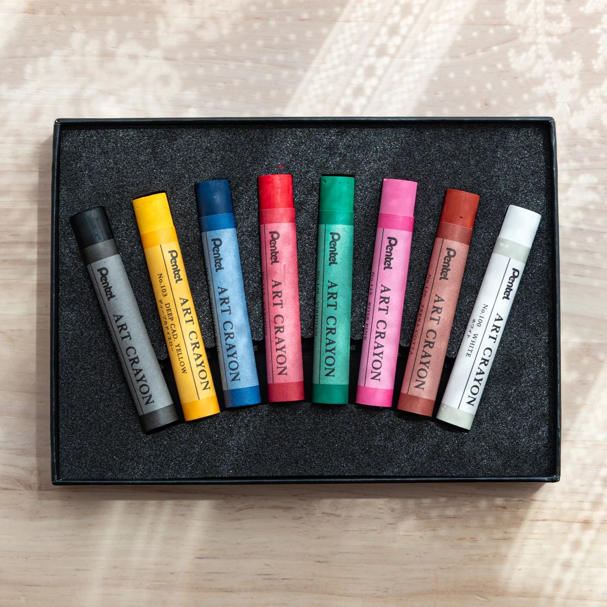 Open Pentel Art Crayon box showing 8 sticks in black foam tray: viridian, carmine, prussian blue, rose pink, and terra cotta