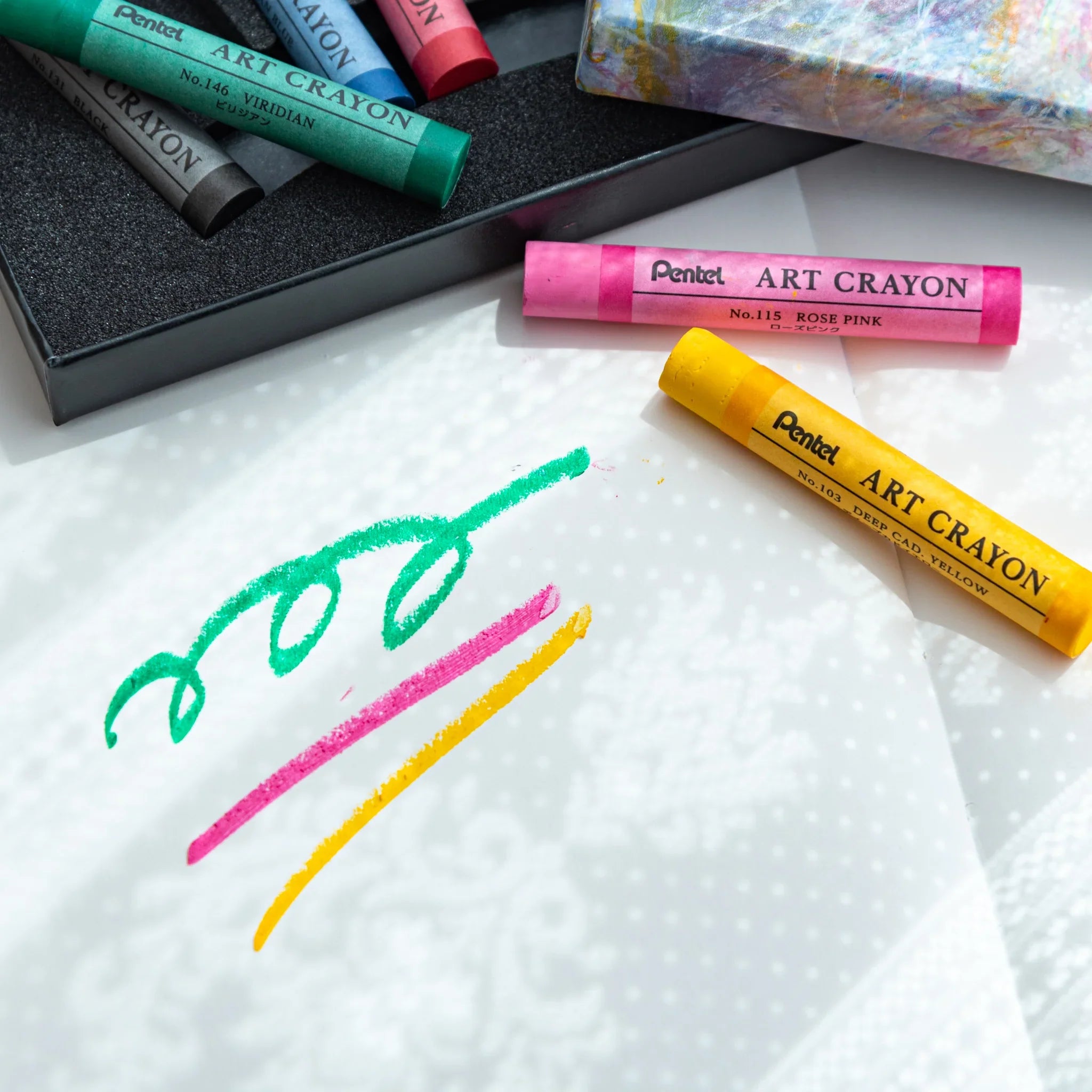 Rose pink and deep cadmium yellow Pentel Art Crayons on white paper beside green, pink, and yellow crayon marks