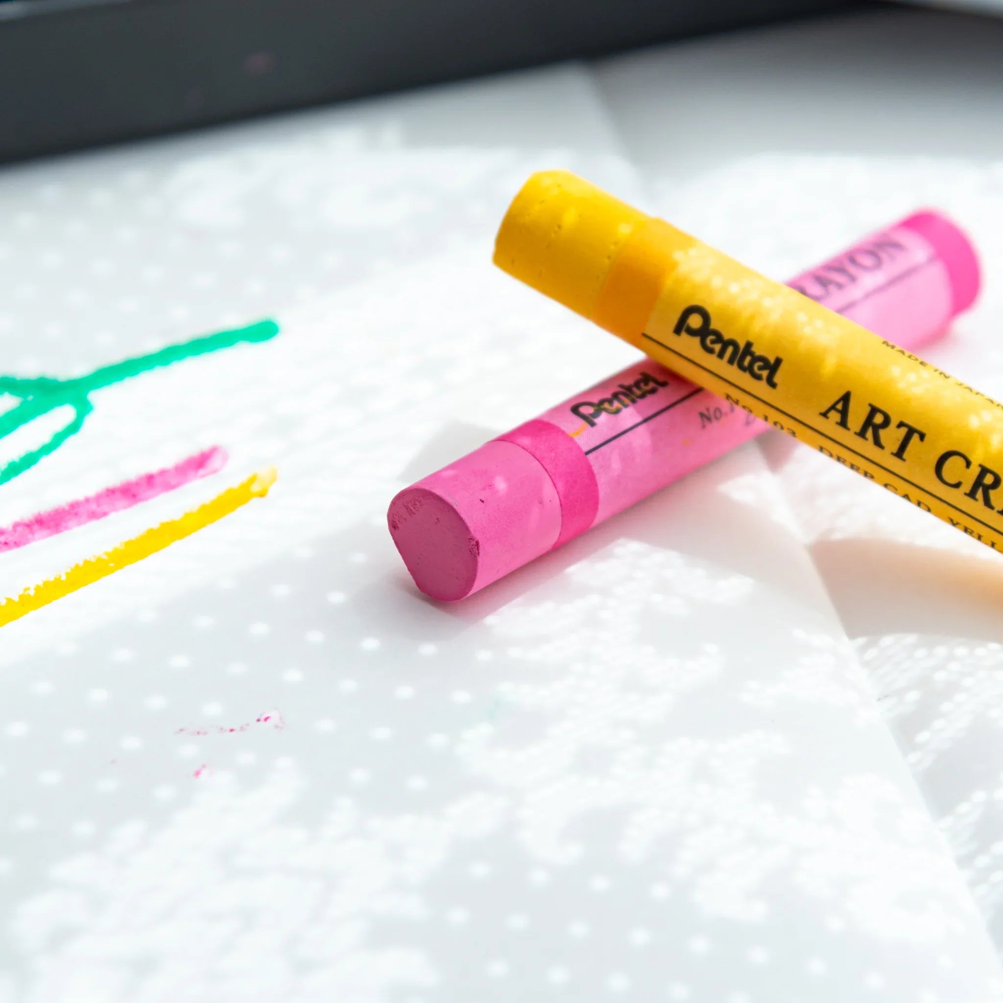 Pink and yellow Pentel Art Crayons on dotted paper with green and pink lines; Japanese crayon set by Pentel