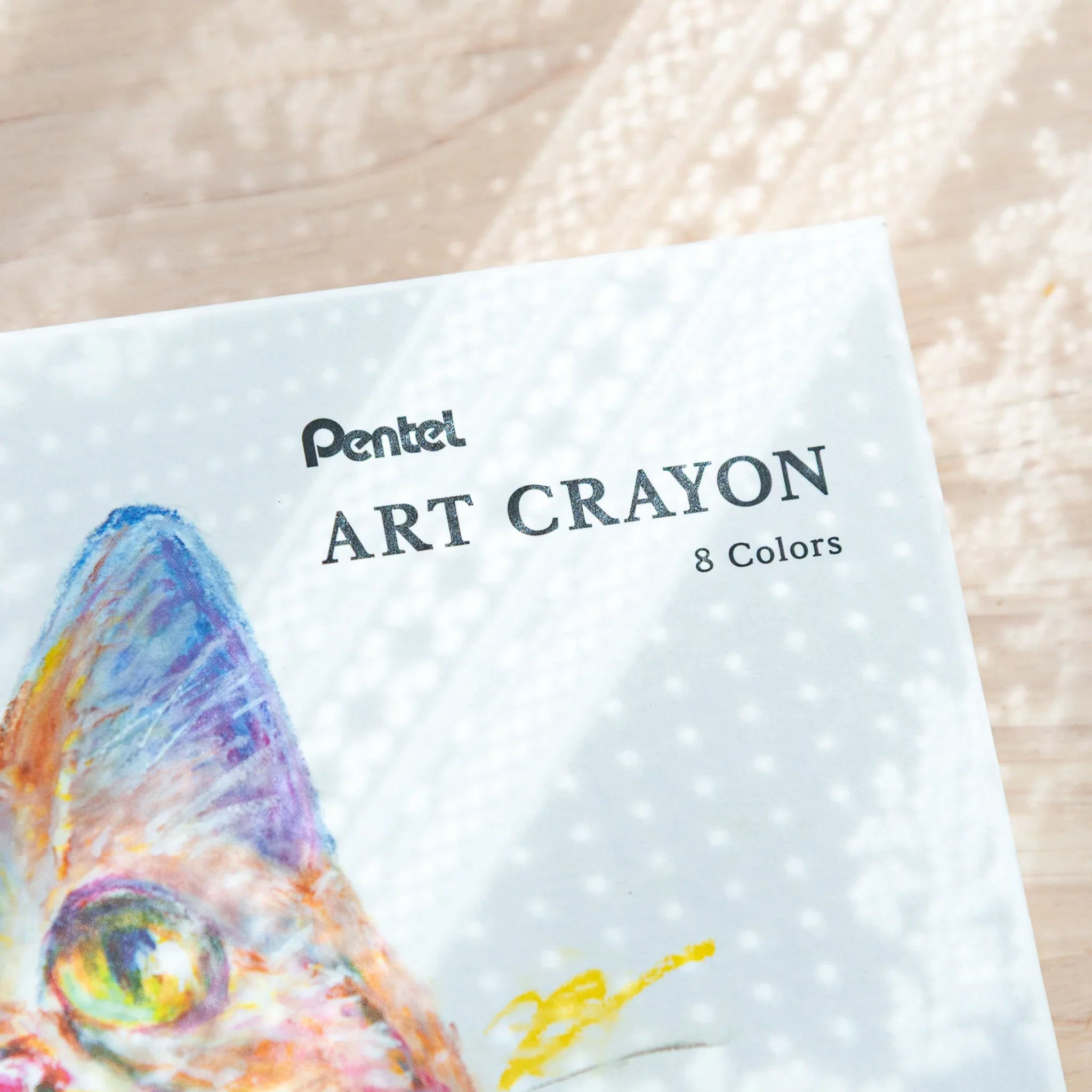 Close-up of Pentel ART CRAYON 8 Colors box upper corner with colorful fish artwork and brand text on dotted background