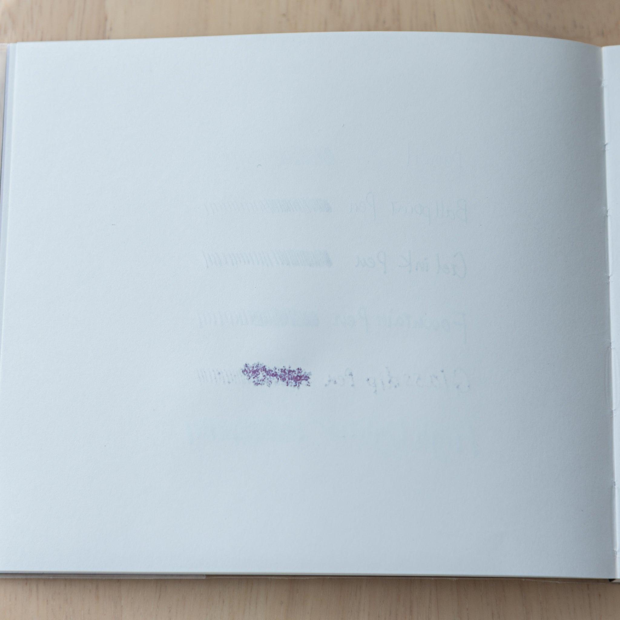 A blank notebook page showing ink bleed-through from the other side, faintly revealing pen test marks.