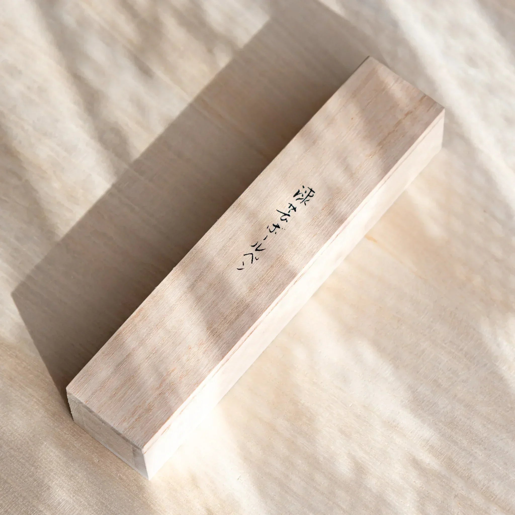 Angled wooden box with Japanese script for a Japanese Ballpoint Pen placed on a desk.