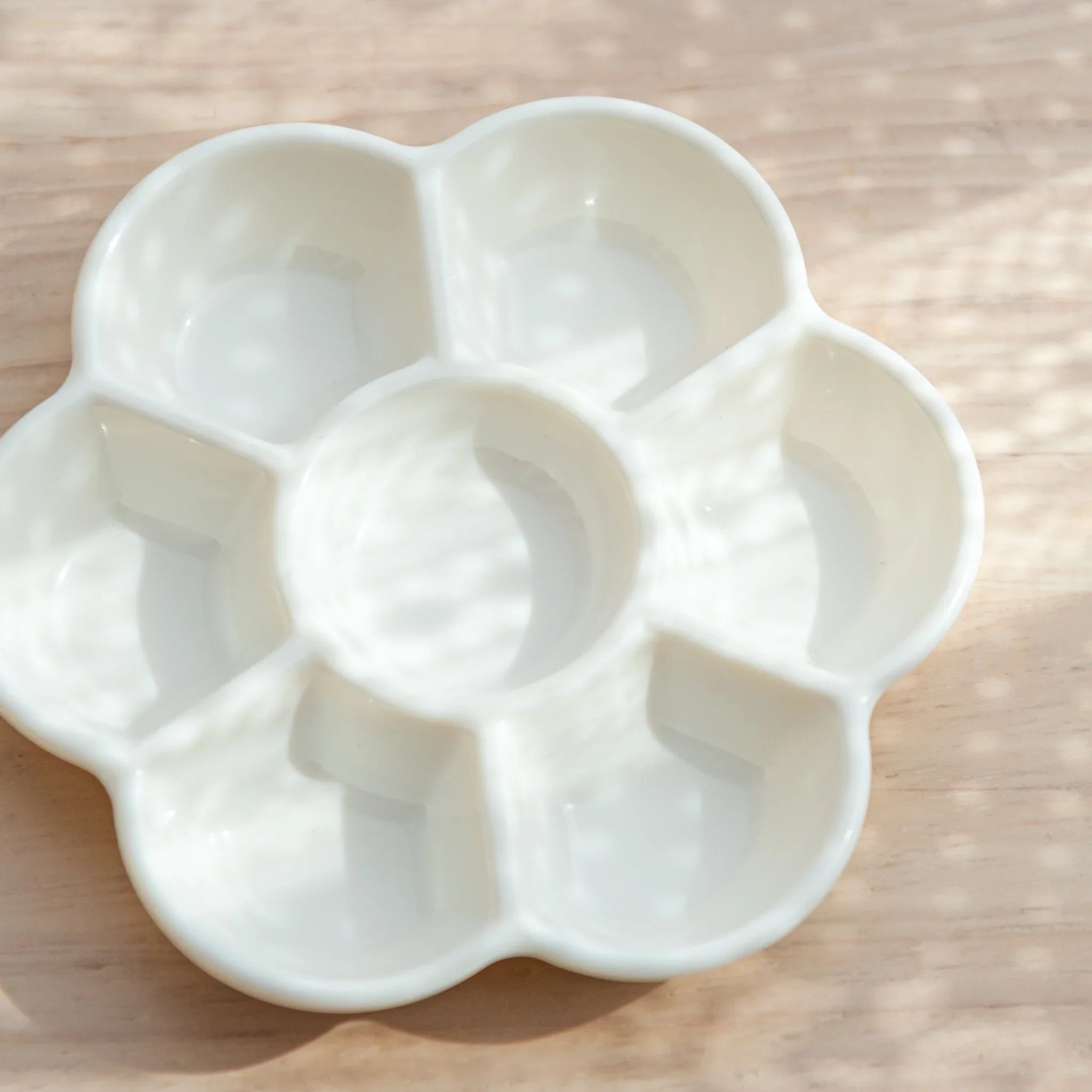 Angled view of white ume flower form paint palette showing multiple shallow wells for watercolor mixing
