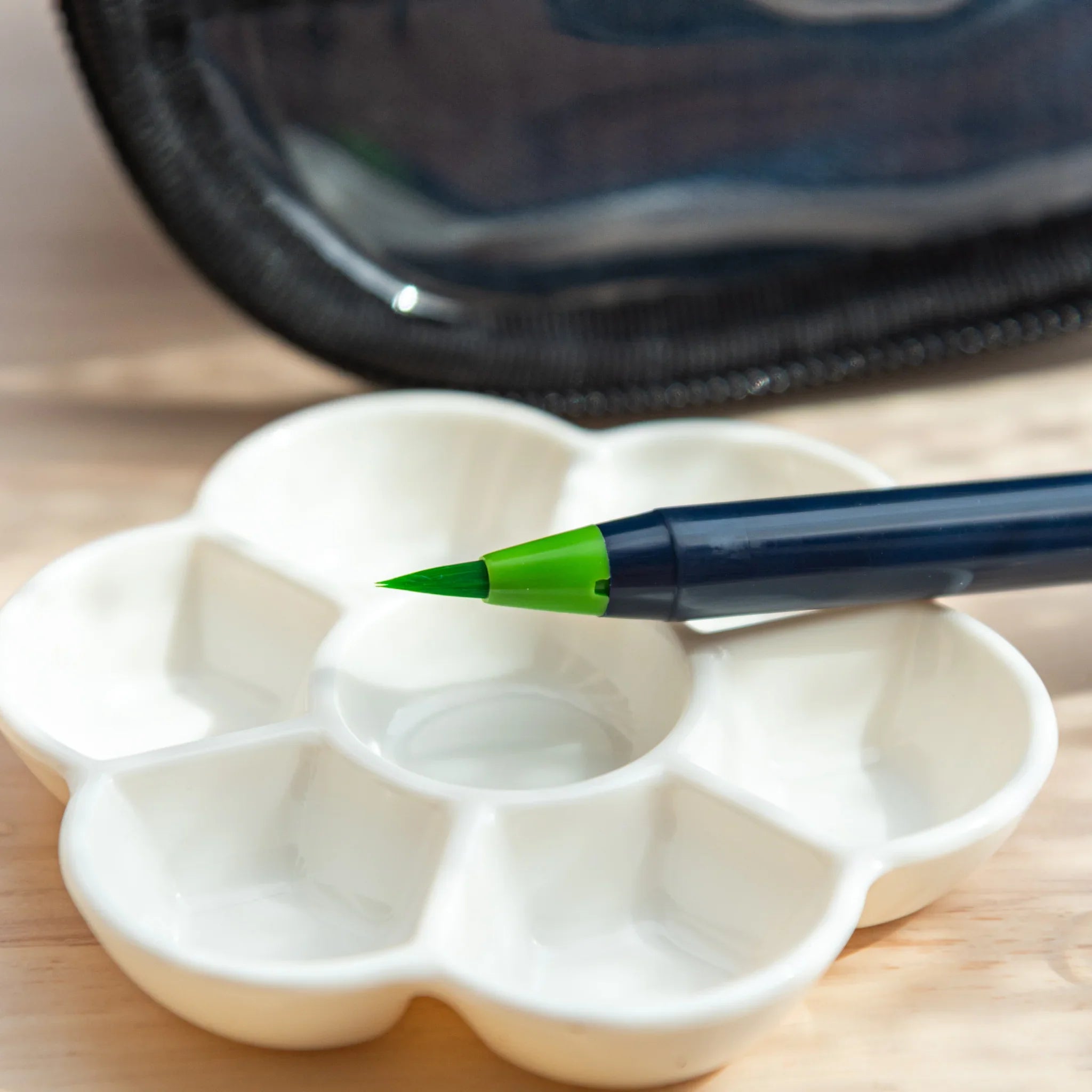 Close-up of green Sai brush pen resting on a white flower-shaped palette, used for arts and crafts painting.