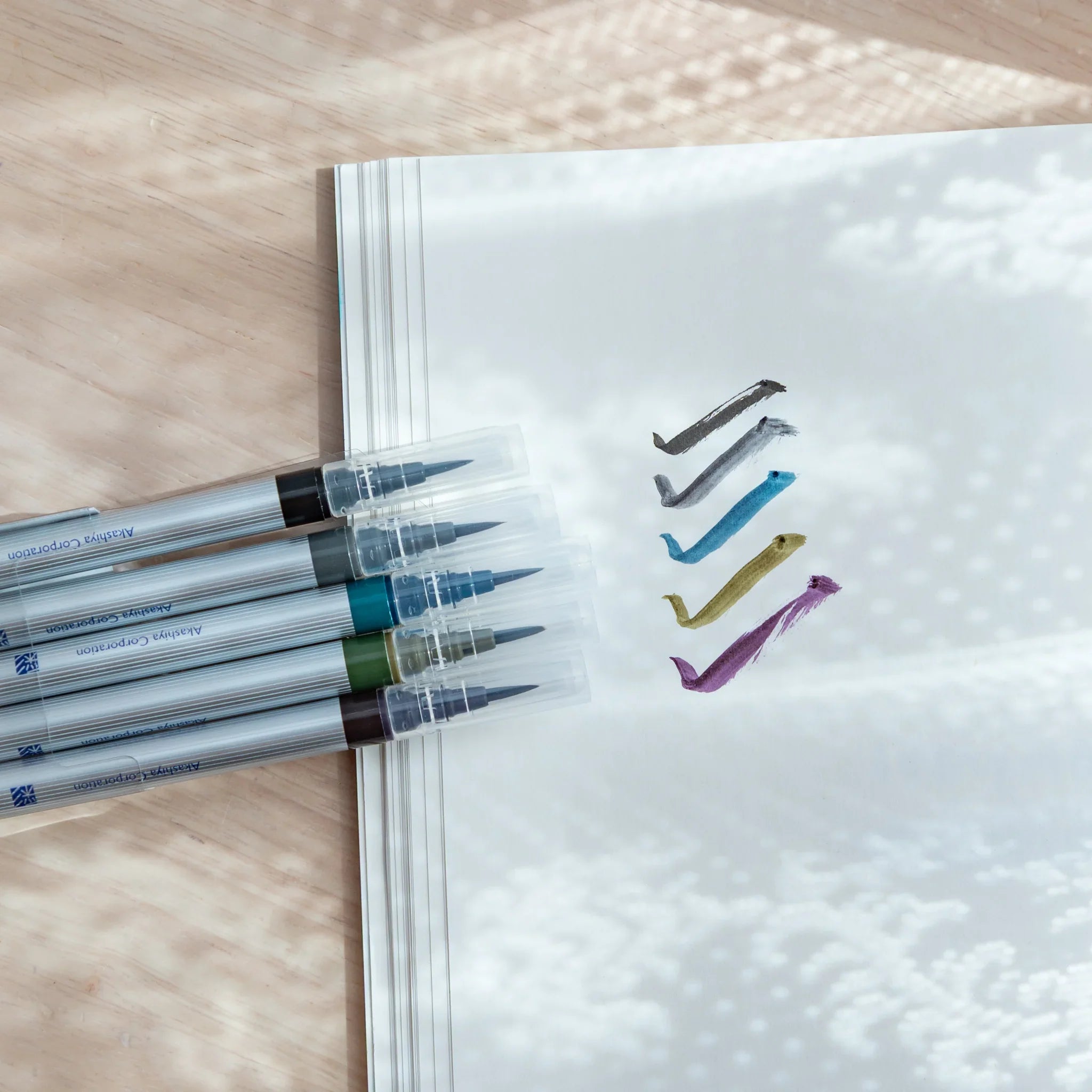 Five dark colored brush pens showing rich deep blue, purple, red, brown and black pigment watercolor tones