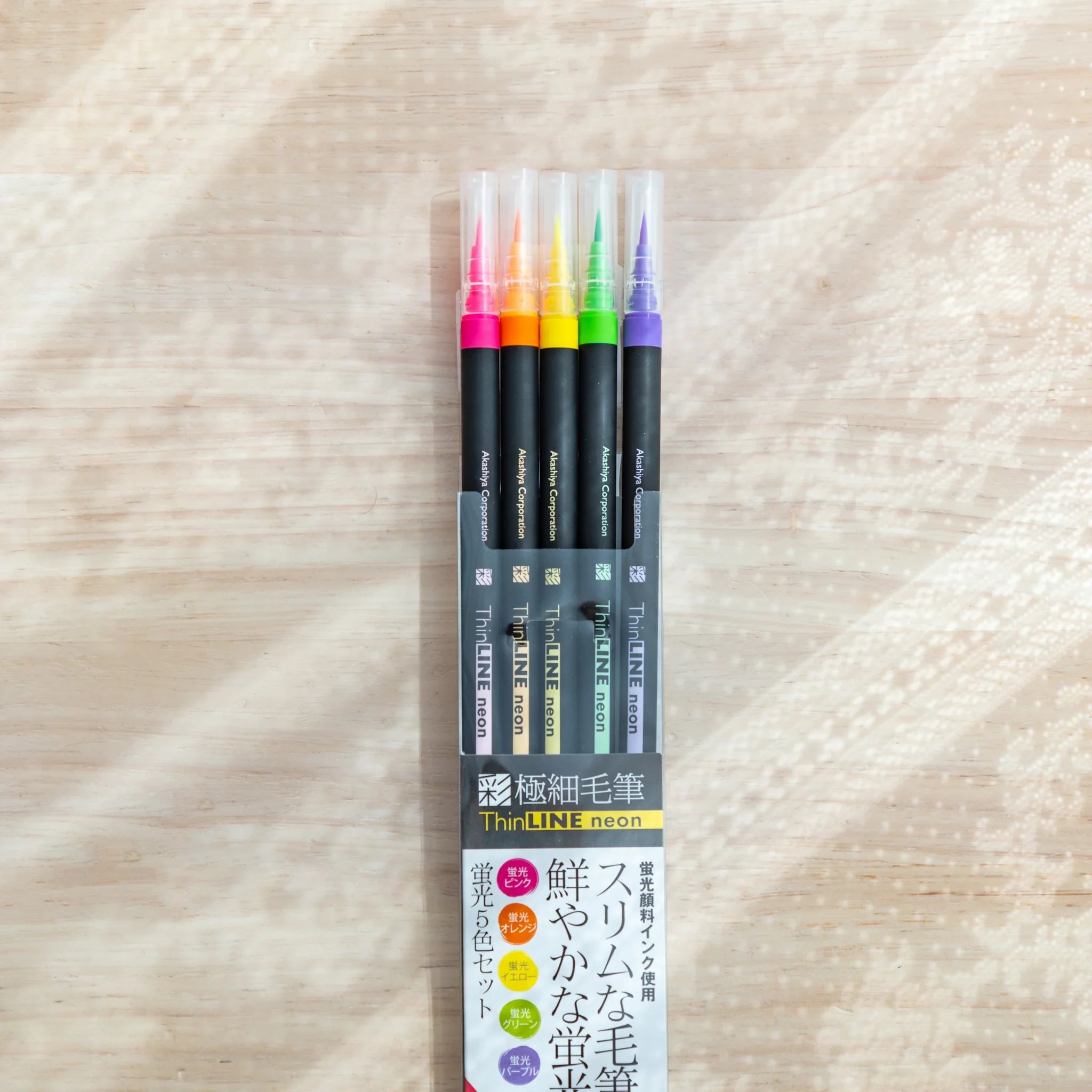 Five bright neon colored brush pens displaying fluorescent pink, yellow, orange, green and bright blue tones