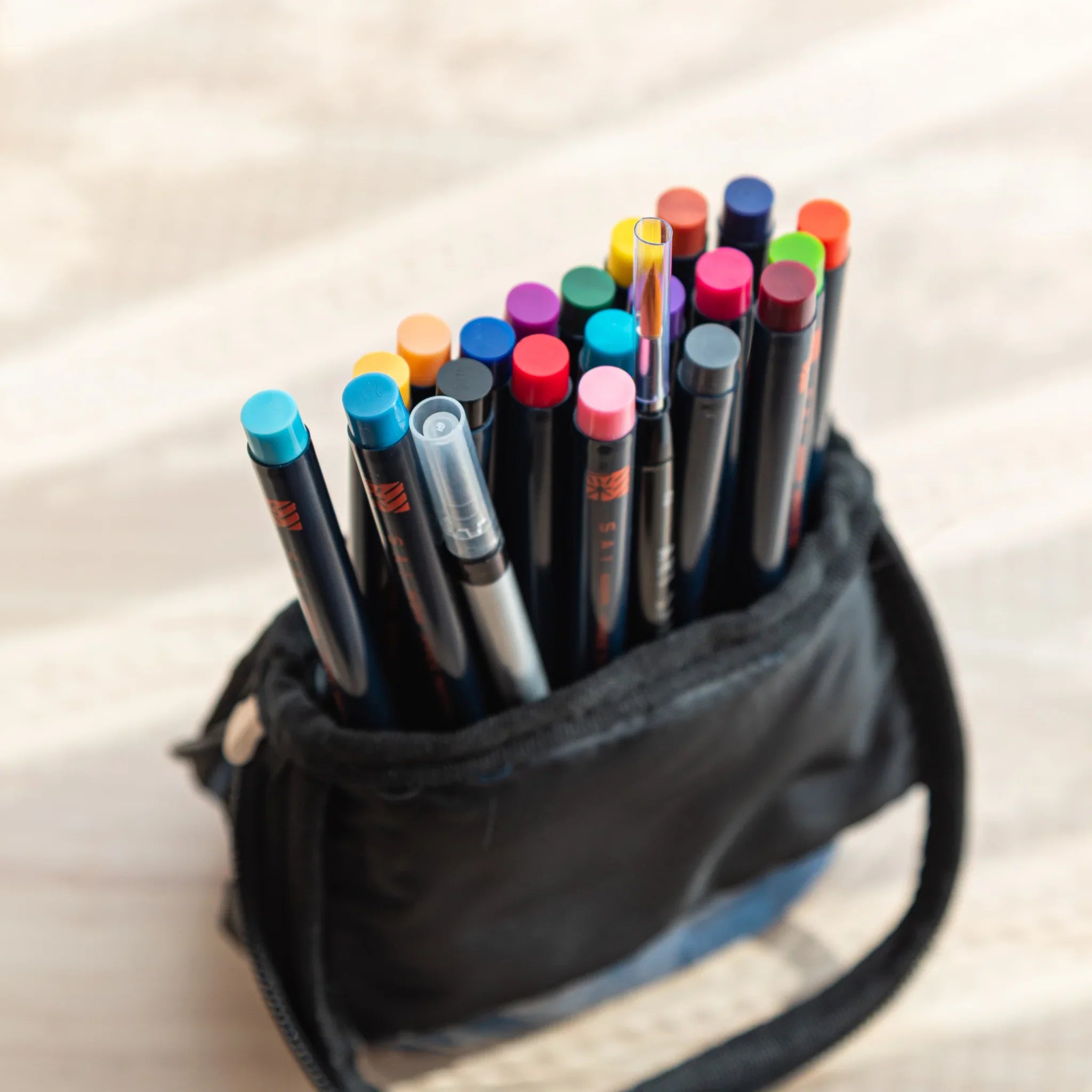 Opened denim case revealing organized watercolor brush pens and accessories for complete painting kit