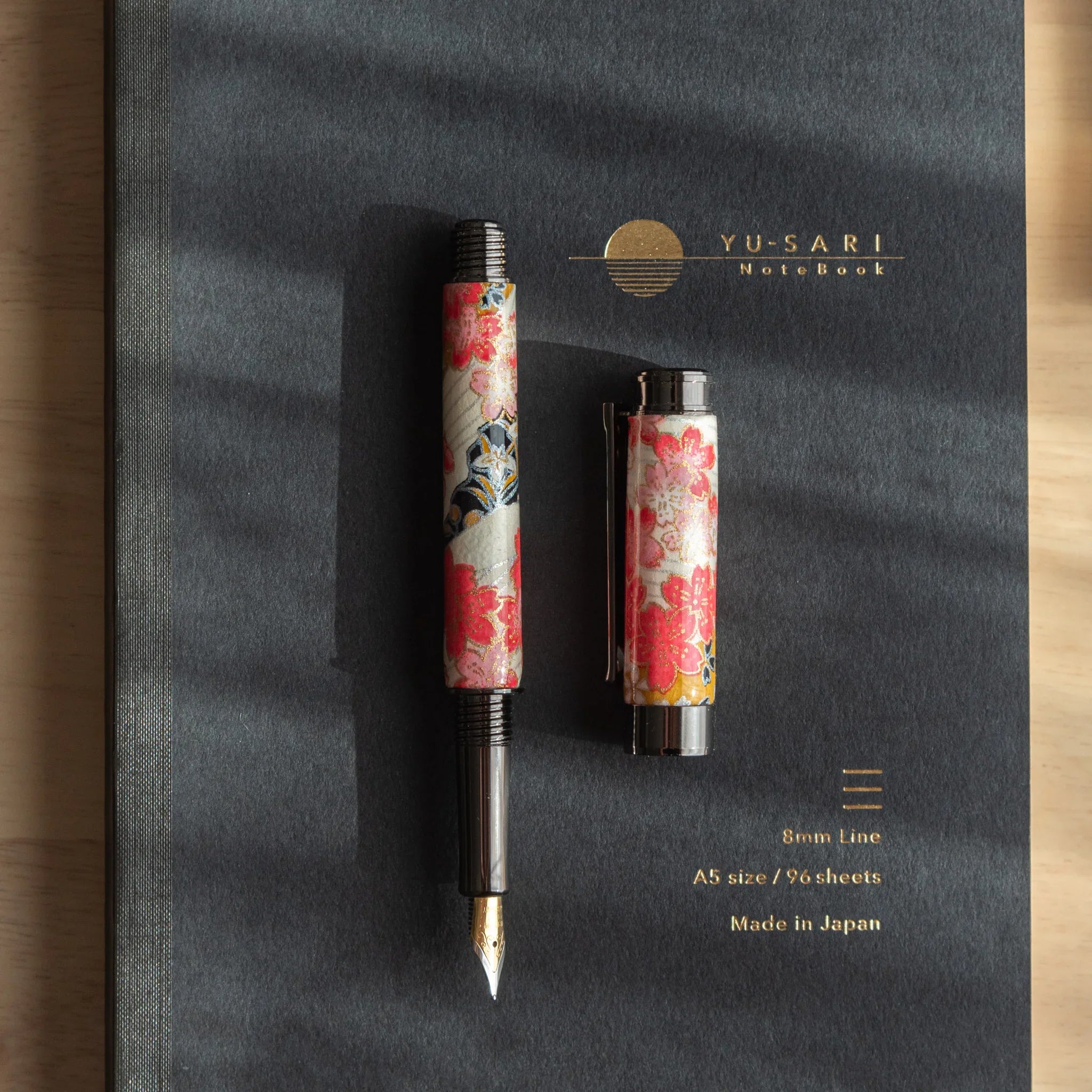 Akebono Cherry Mino Washi fountain pen cap and metallic components displayed on red botanical wrapper angled view