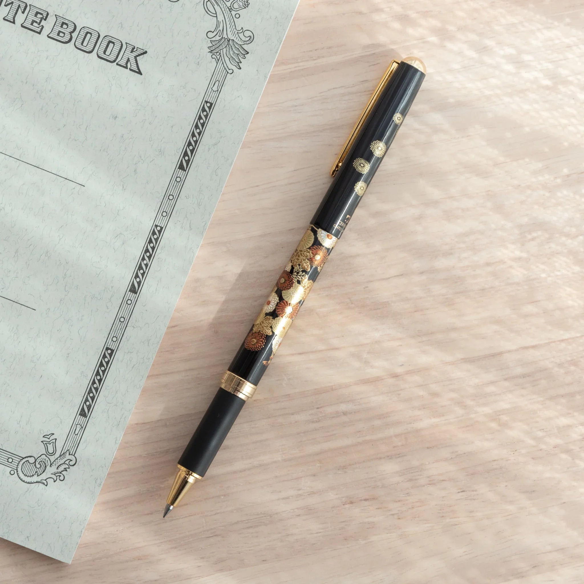 Japanese Ballpoint Pen with gold floral design resting with a notebook.