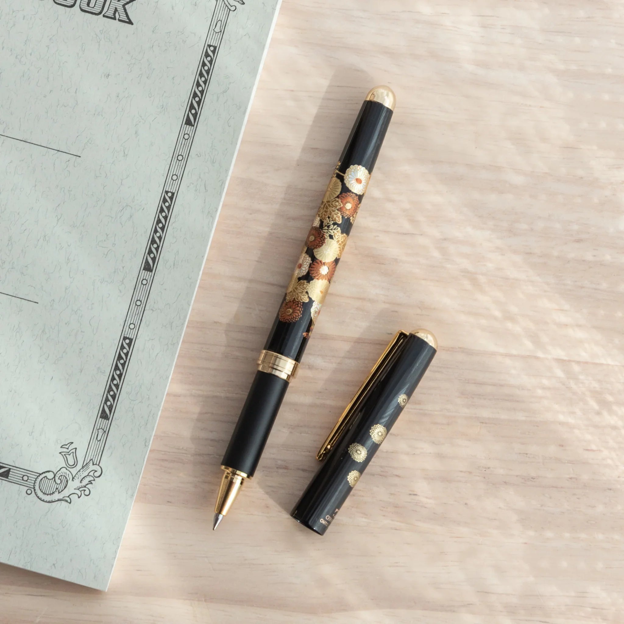 Capped-off Japanese Ballpoint Pen with Lacquer finish, featuring golden chrysanthemum design on a black glossy body.