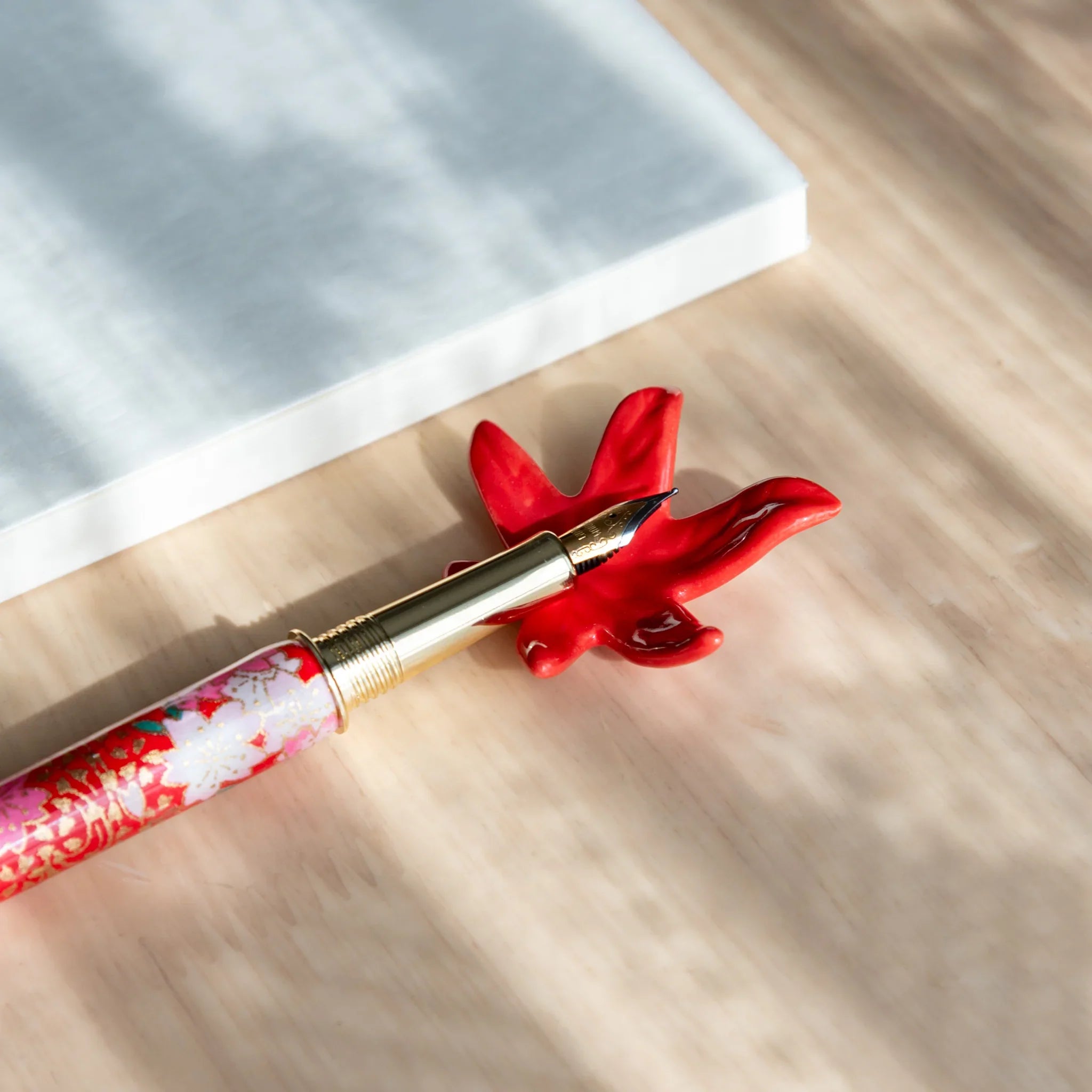 Red maple leaf shaped pen rest in warm fall tones with detailed carved leaf vein structure showing seasonal design theme