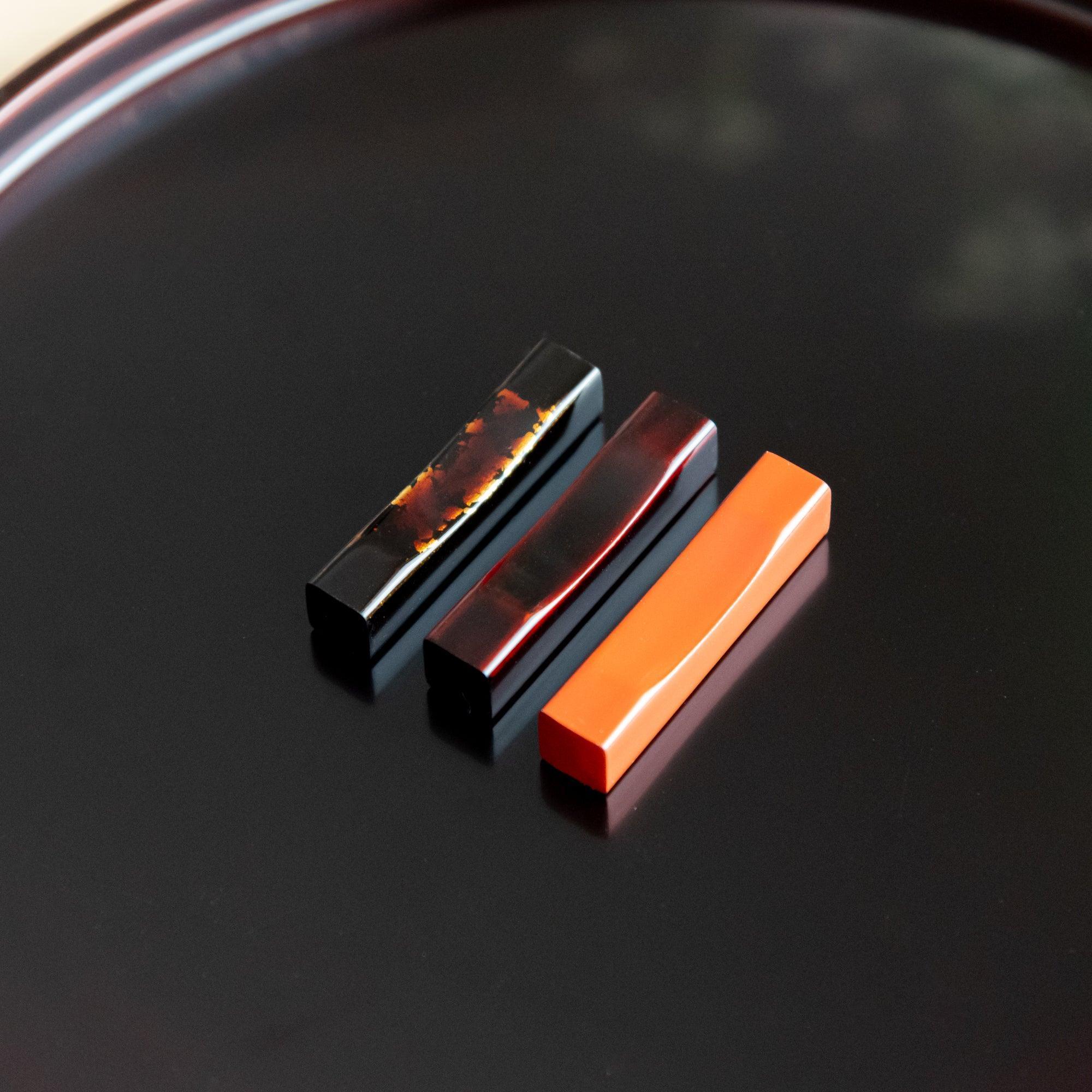 Traditional Echizen lacquer pen rest features black glaze with sakura wood base and gold inlay, keeping pens secure during