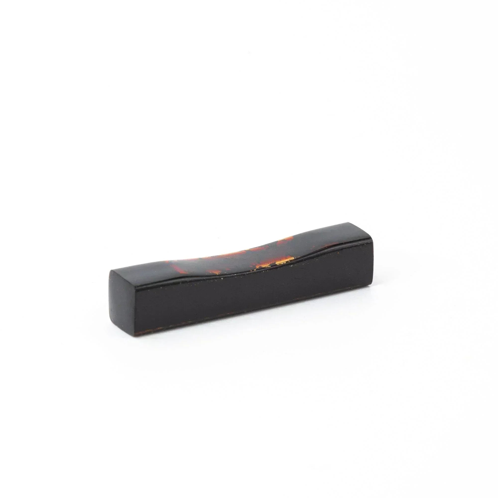 A single black and red marbled Japanese stationery pen rest with a curved design against a white background.
