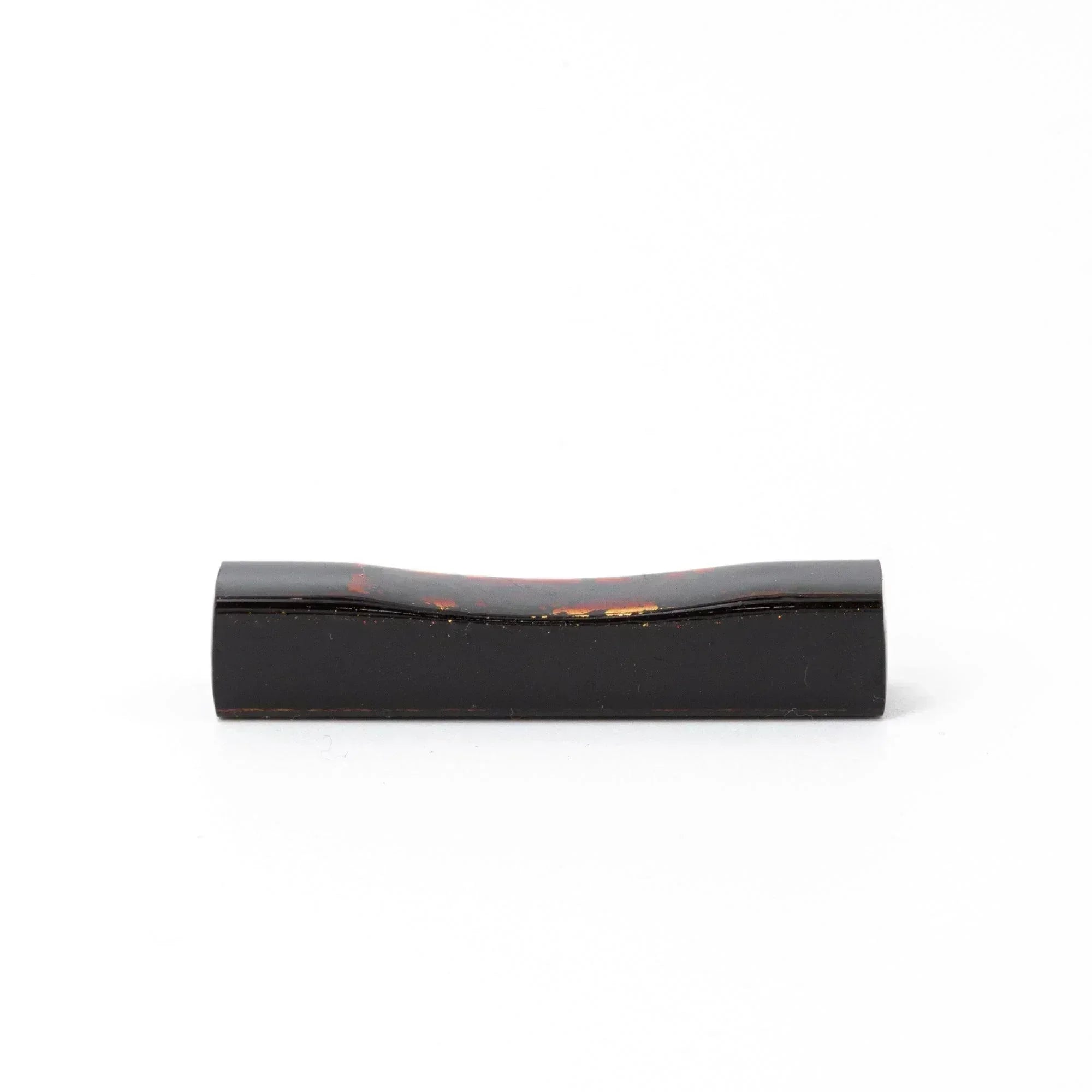 A single black and red marbled Japanese stationery pen rest with a curved design against a white background.