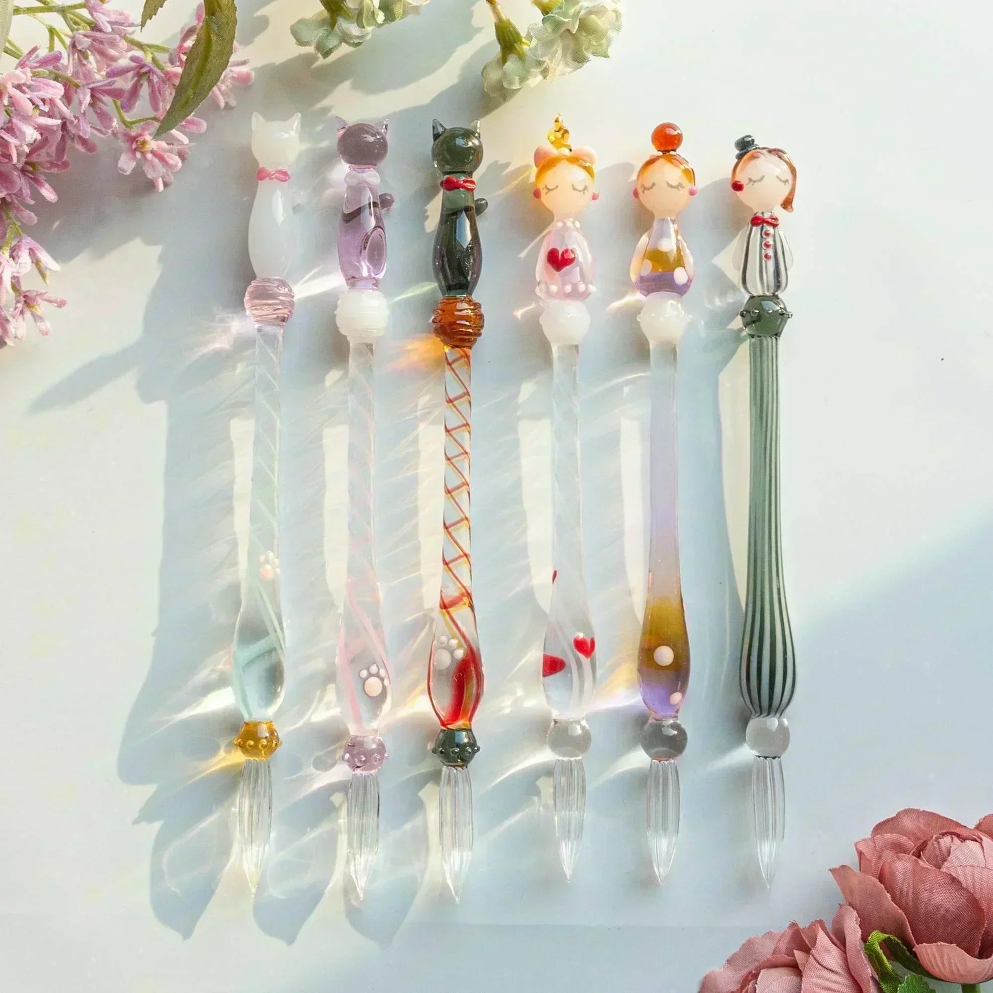 A whimsical set of glass dip pens featuring cats and human figures, capturing the charm of their playful designs