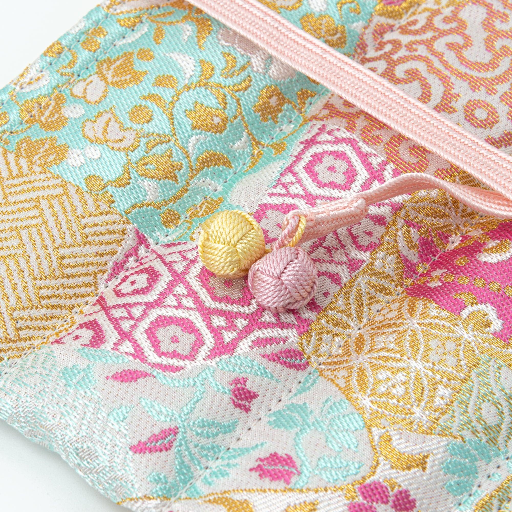 A close-up of a Japanese fountain pen case made of Nishijin silk, highlighting the intricate floral and geometric patterns and decorative pink cord.