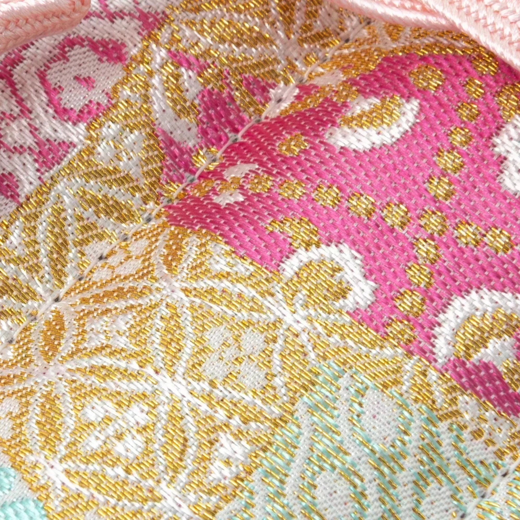 A close-up of a Japanese fountain pen case made of Nishijin silk, highlighting intricate gold and pink floral and geometric woven patterns.