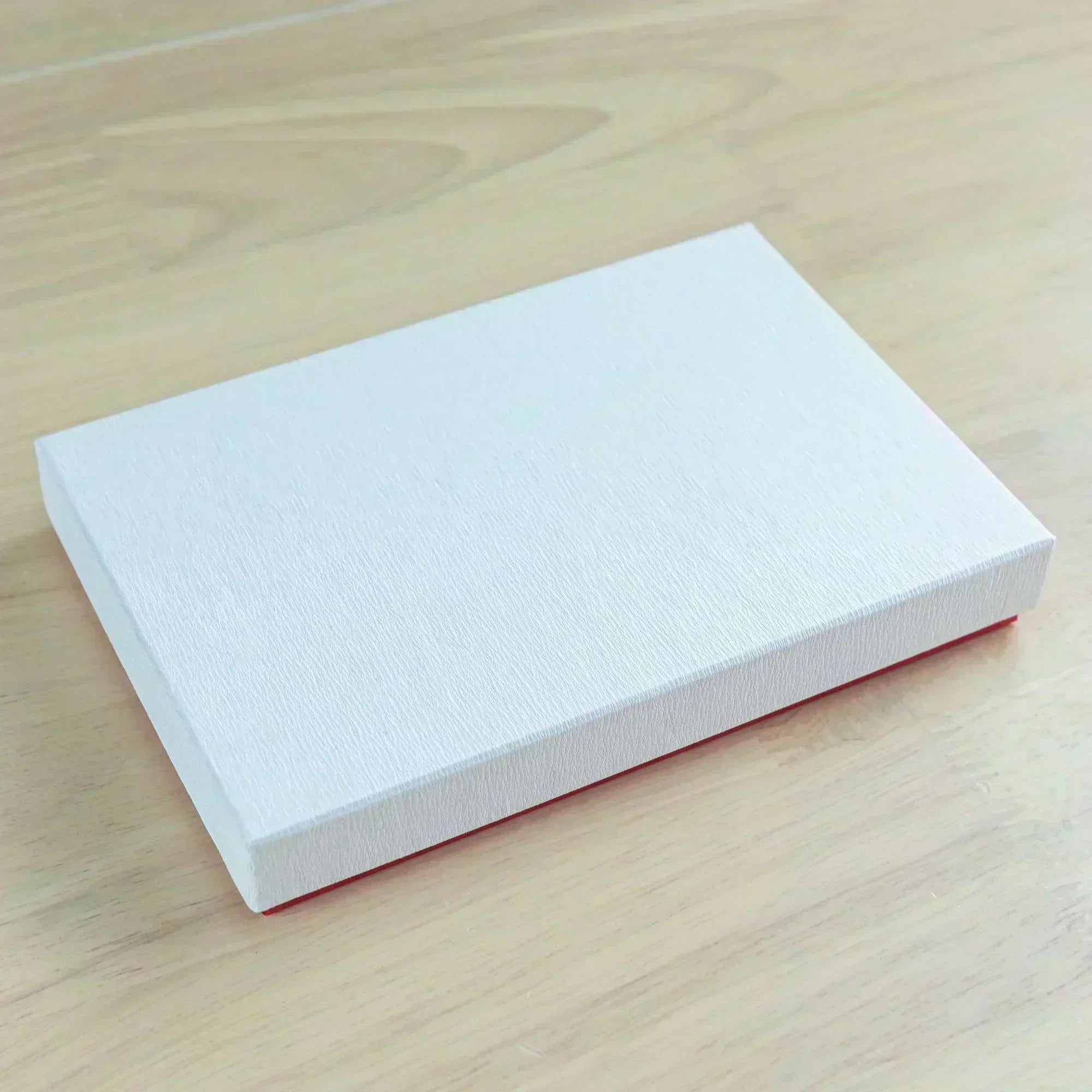 A white textured box on a wooden surface, likely packaging for the Japanese fountain pen case or related stationery.